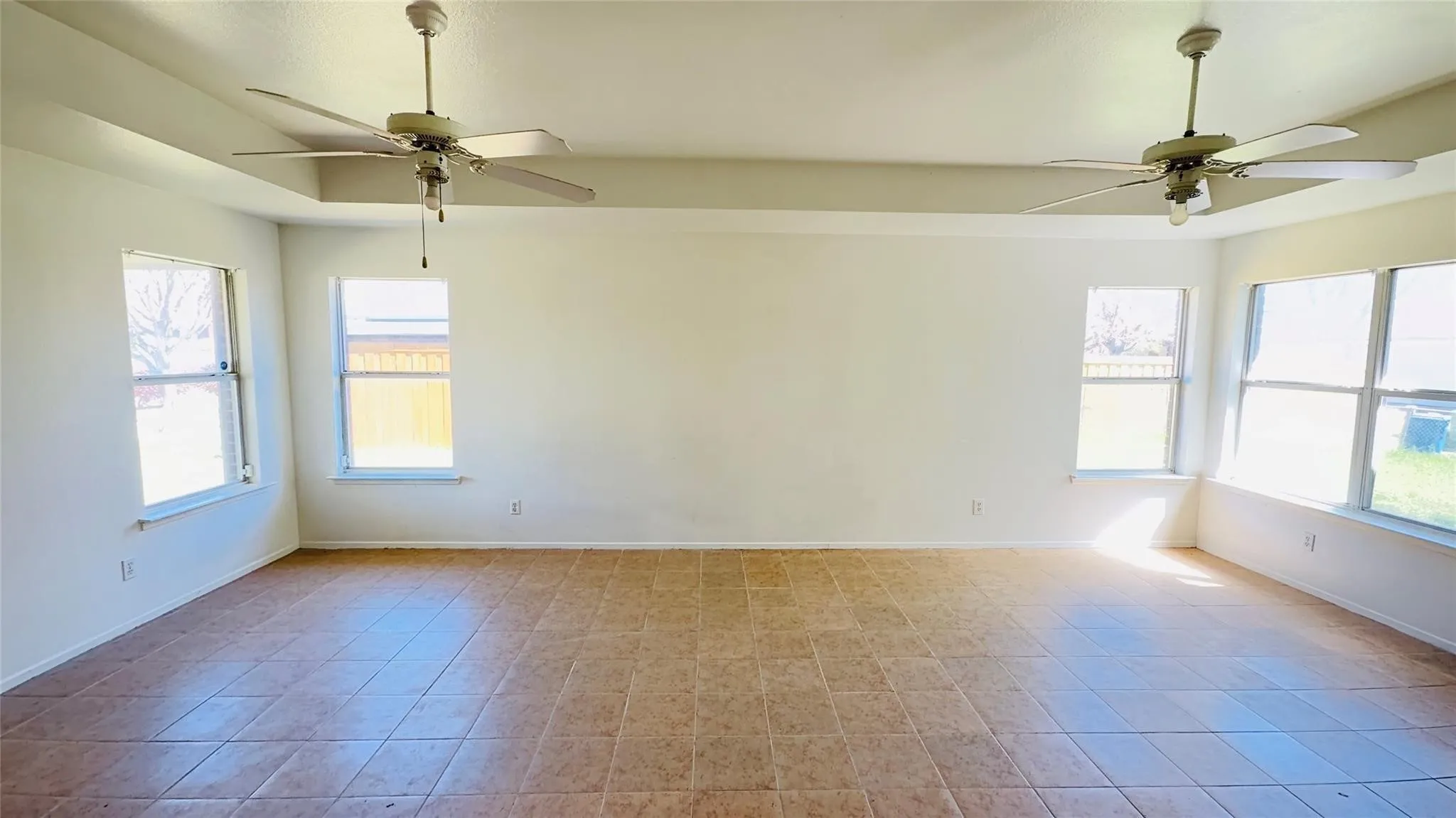 Spacious room featuring tile flooring, multiple windows, two ceiling fans, and a tray ceiling