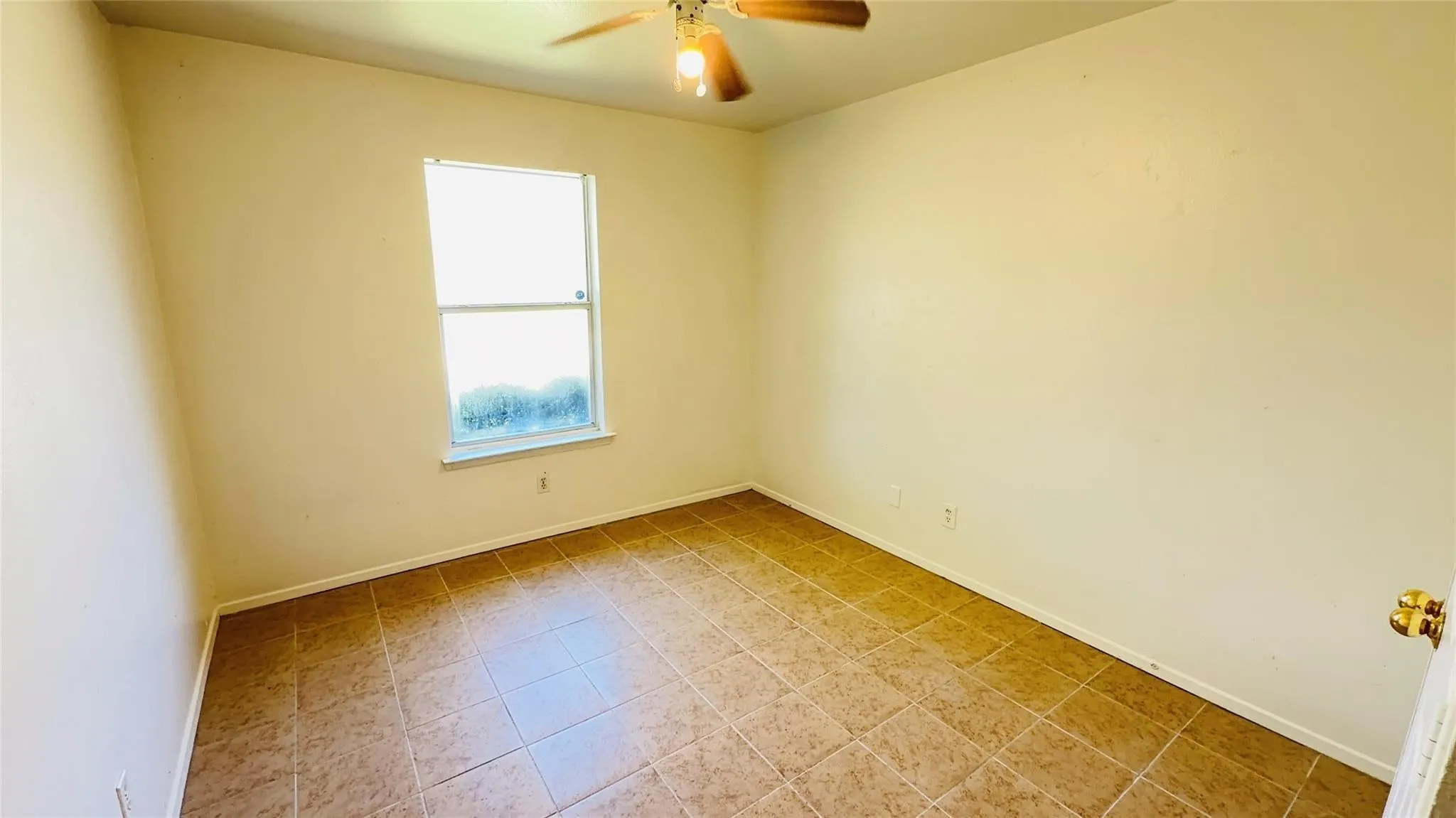 Warm-toned tile flooring, light neutral wall paint, single window, and ceiling fan with integrated lighting