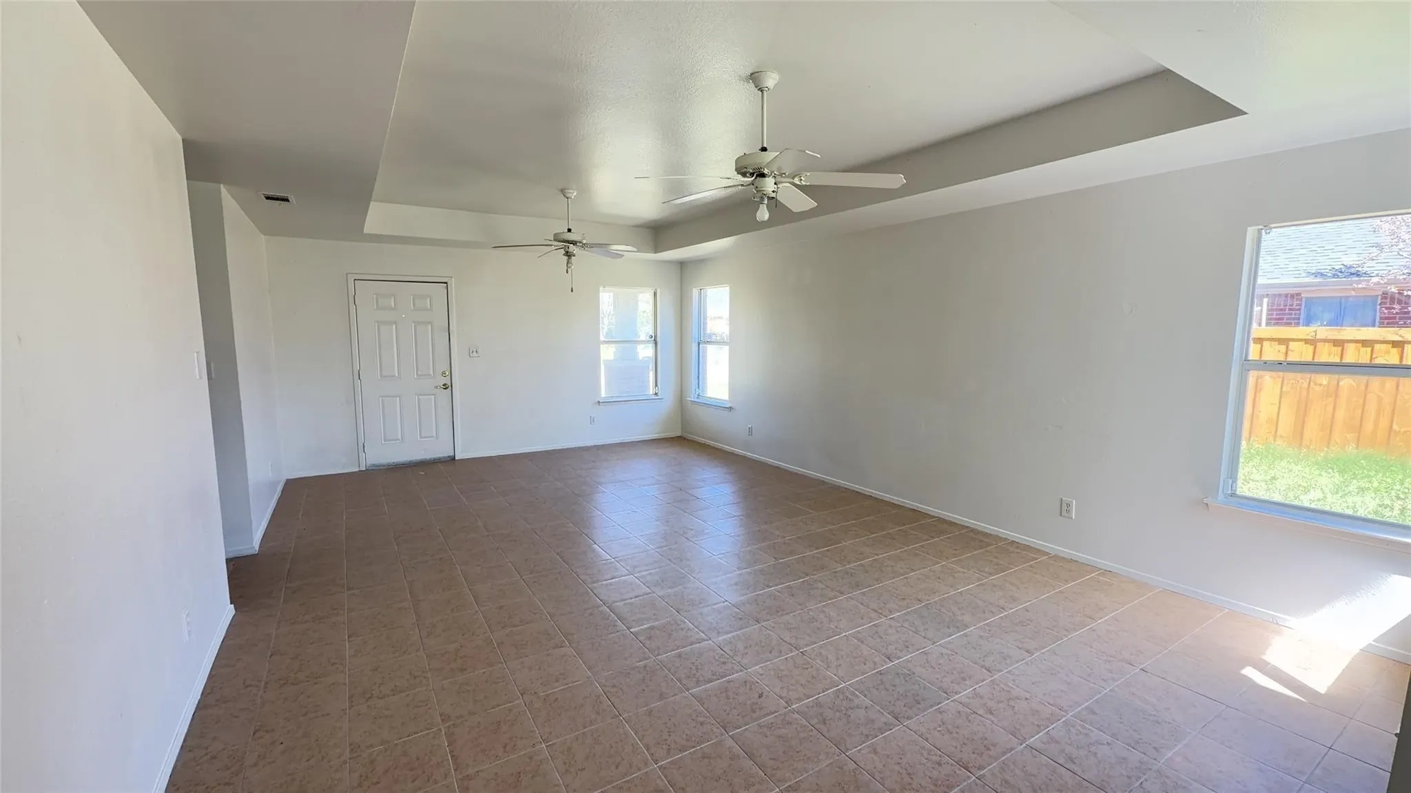 Tray ceiling with two ceiling fans, ceramic tile flooring, and multiple windows