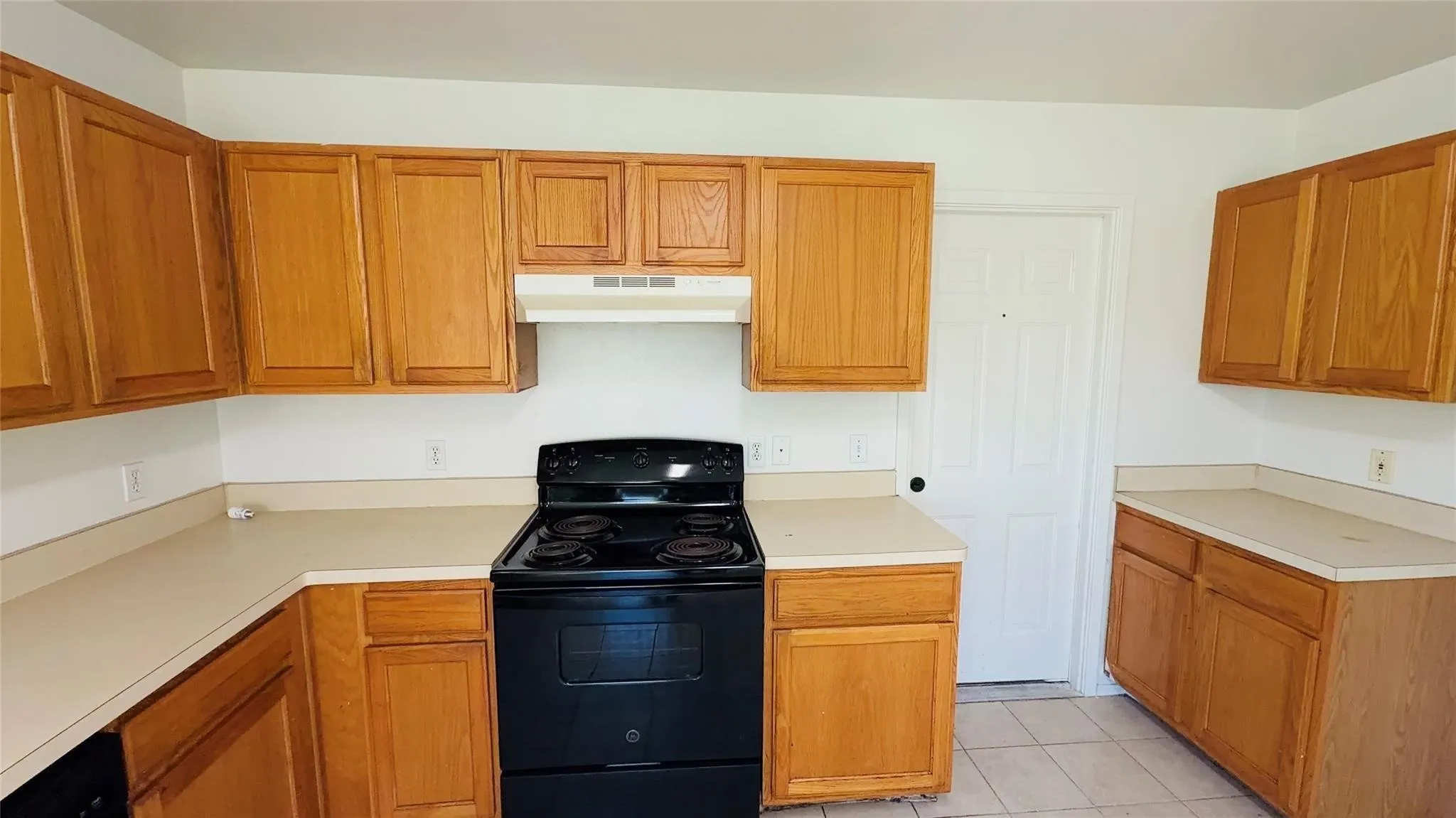 Kitchen with light wood-finish cabinetry, solid surface countertops, and a black electric range
