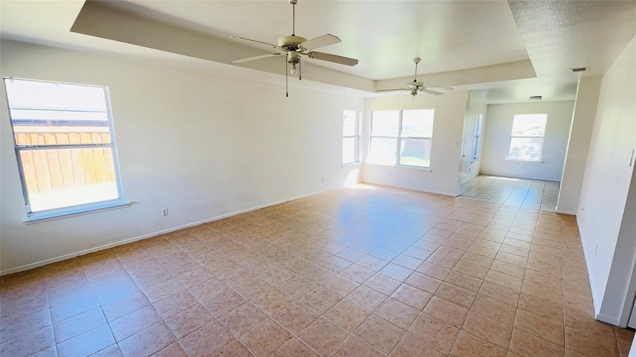 Expansive room featuring tray ceilings, ceiling fans, and tiled flooring