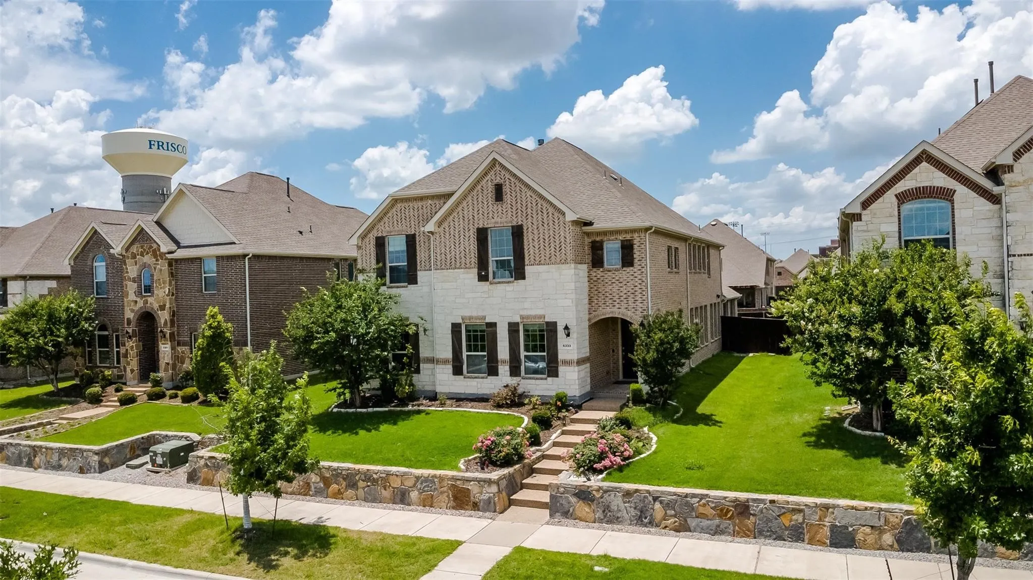 Two-story residence featuring a brick and stone facade, dark-shingle roof, and multiple window shutters