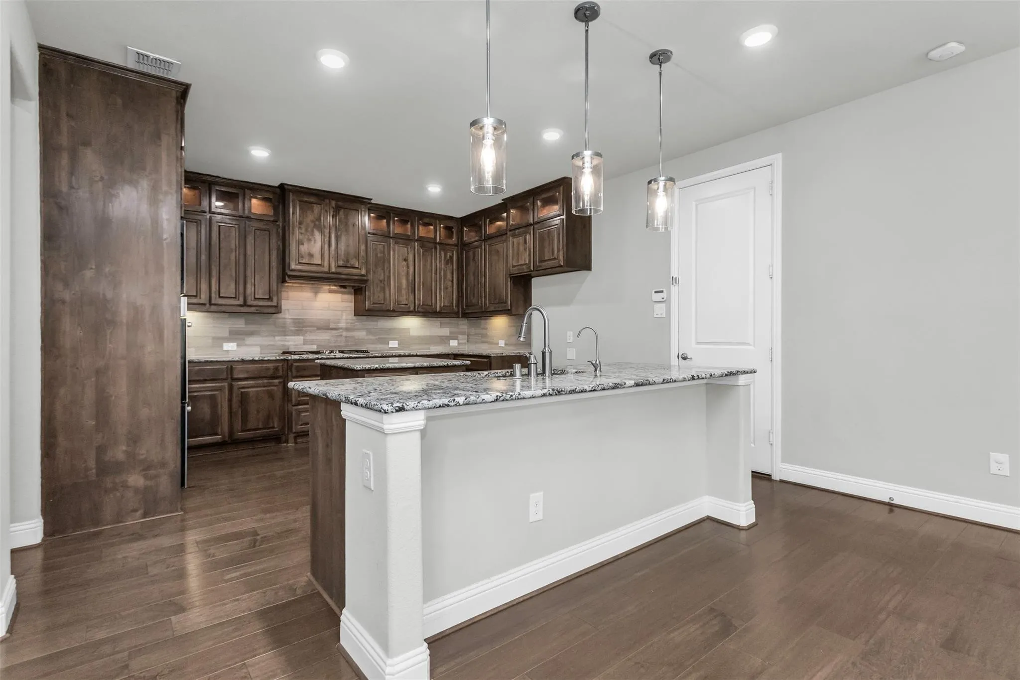 Kitchen featuring dark wood cabinetry, granite countertops, tile backsplash, and wood-finish flooring