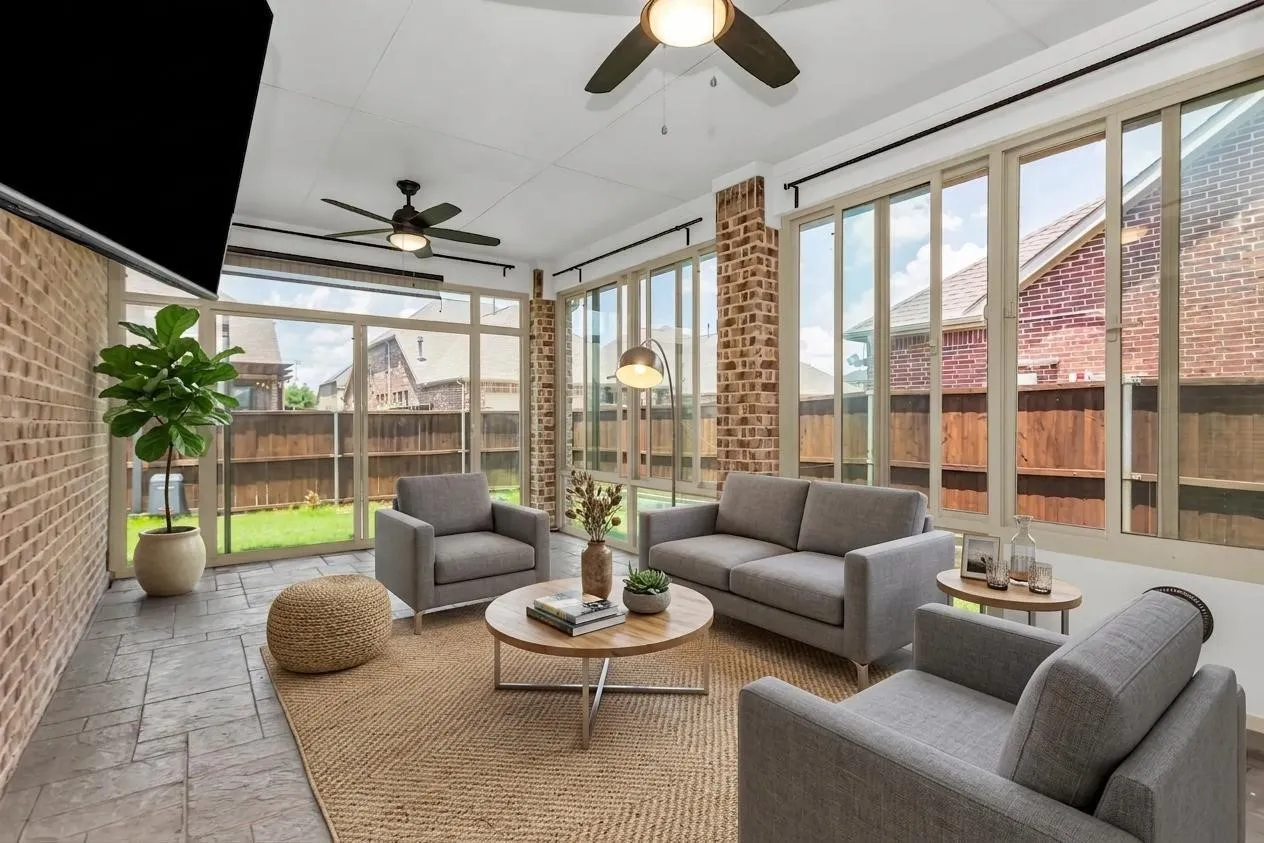 Expansive sunroom featuring brick accent walls, floor-to-ceiling windows, stamped concrete flooring, and ceiling fans