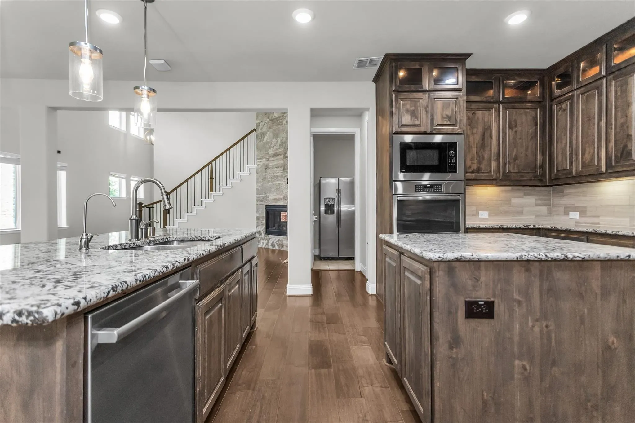 Kitchen featuring wood-finish flooring, granite countertops, stainless steel appliances, pendant lighting, and wood cabinetry