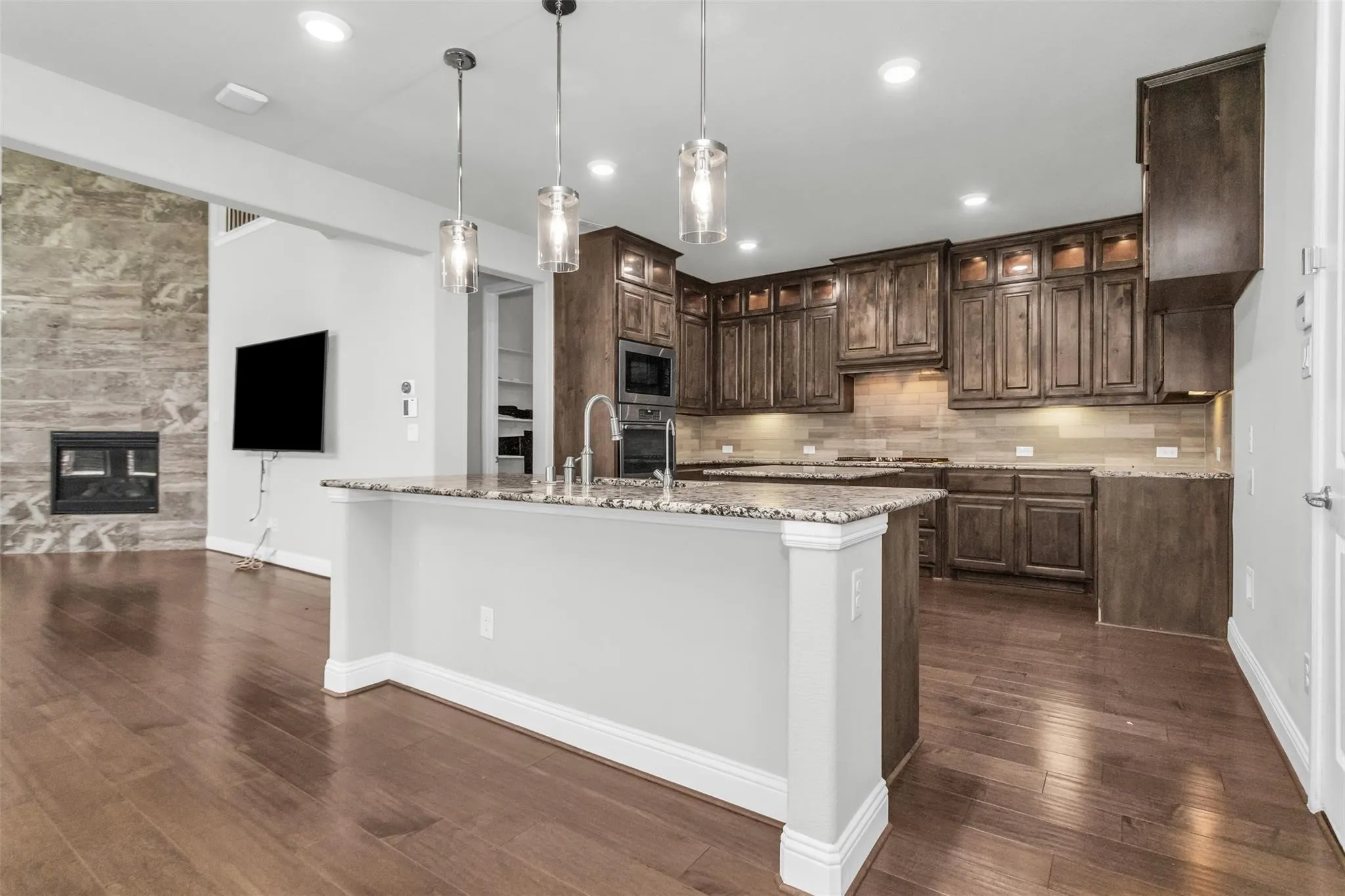 Gourmet kitchen with wood-finish flooring, granite countertops, dark wood cabinetry, and stainless steel appliances