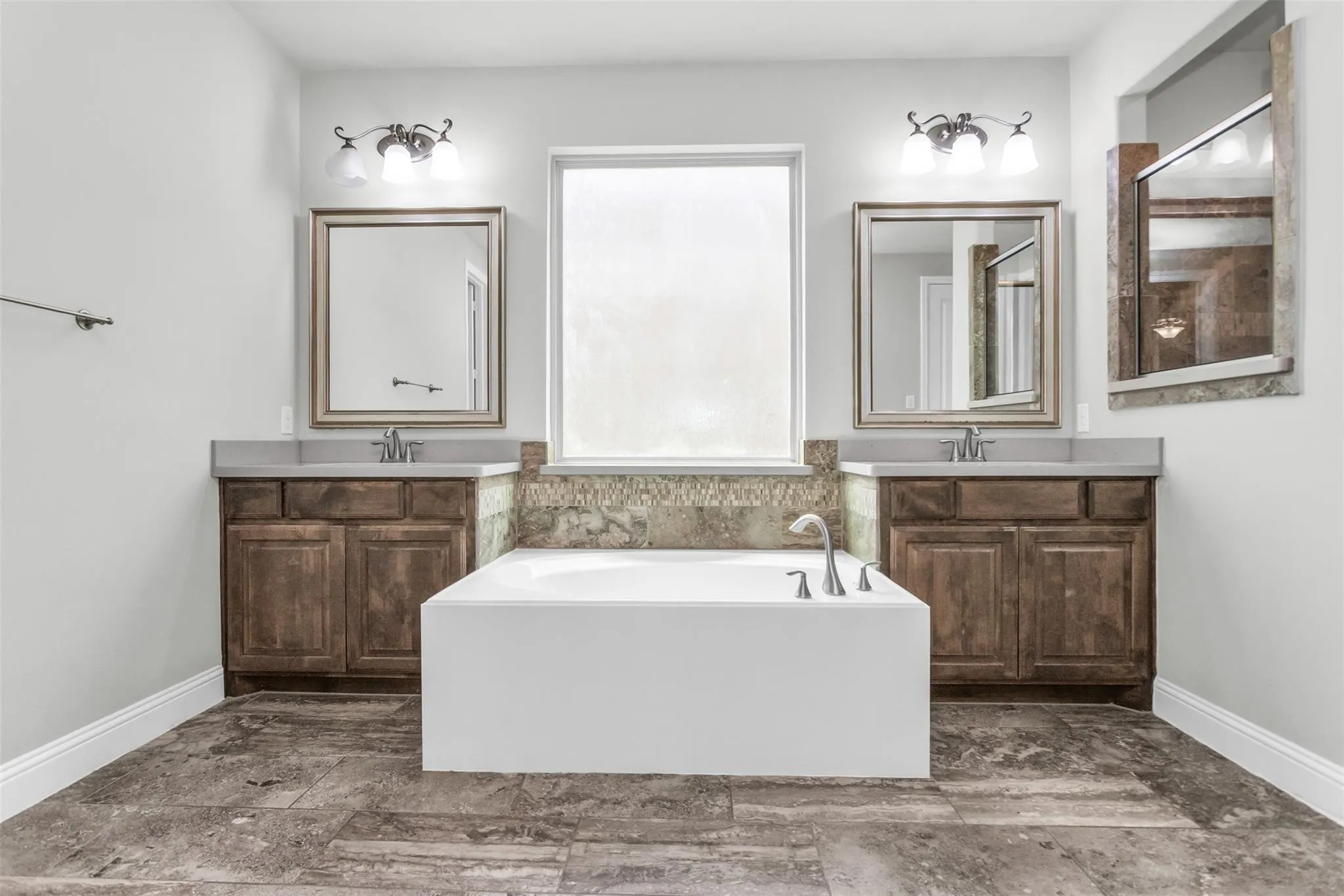 Dual vanities with stone countertops, deep soaking tub, and tile flooring