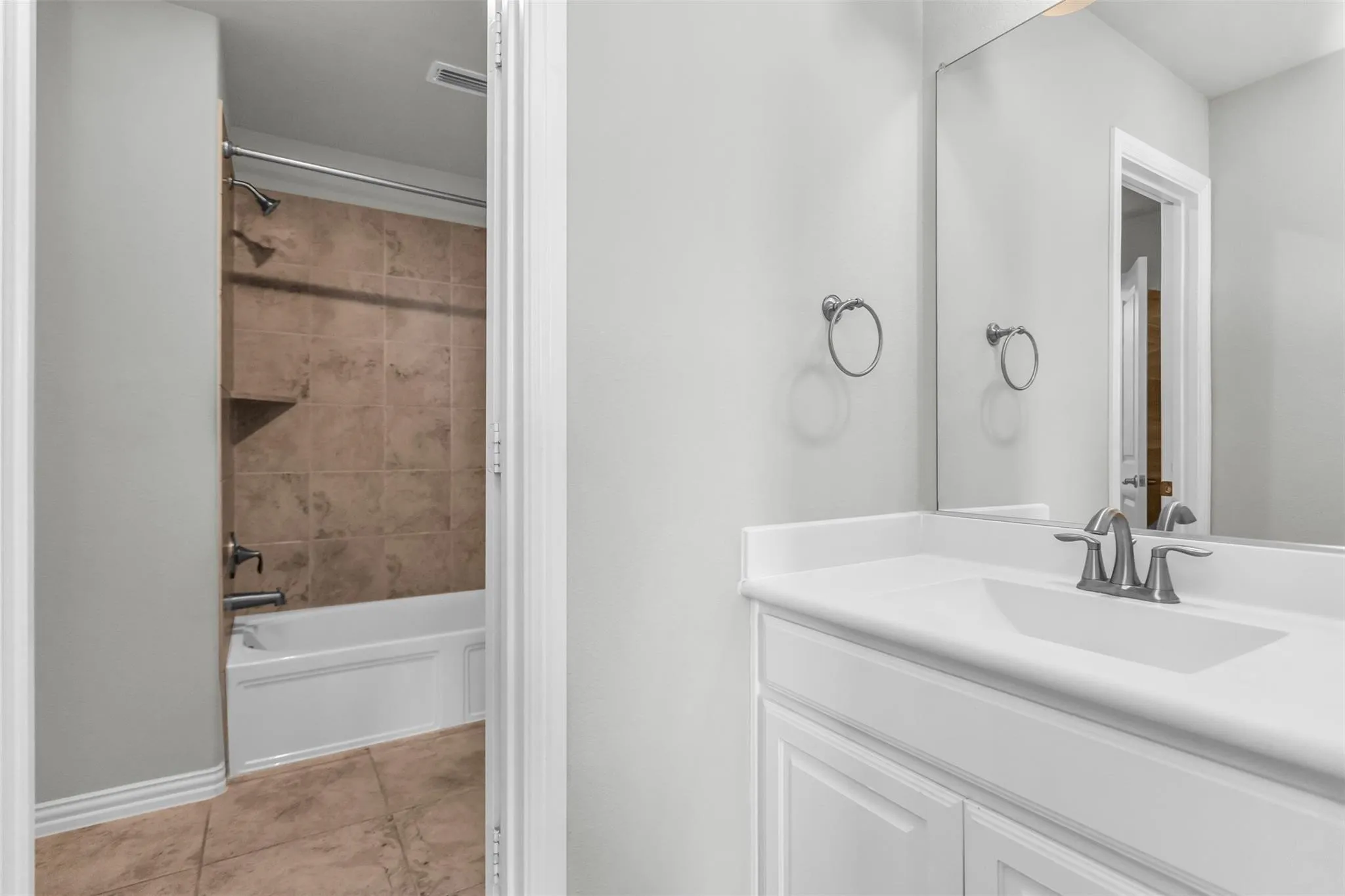 White vanity with integrated sink, brushed nickel faucet, large wall mirror, and tile flooring