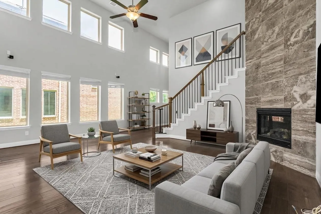 Double-height ceiling with a ceiling fan, a fireplace with a floor-to-ceiling tiled surround, a staircase with dark wood railings and black balusters, and dark wood-finish flooring