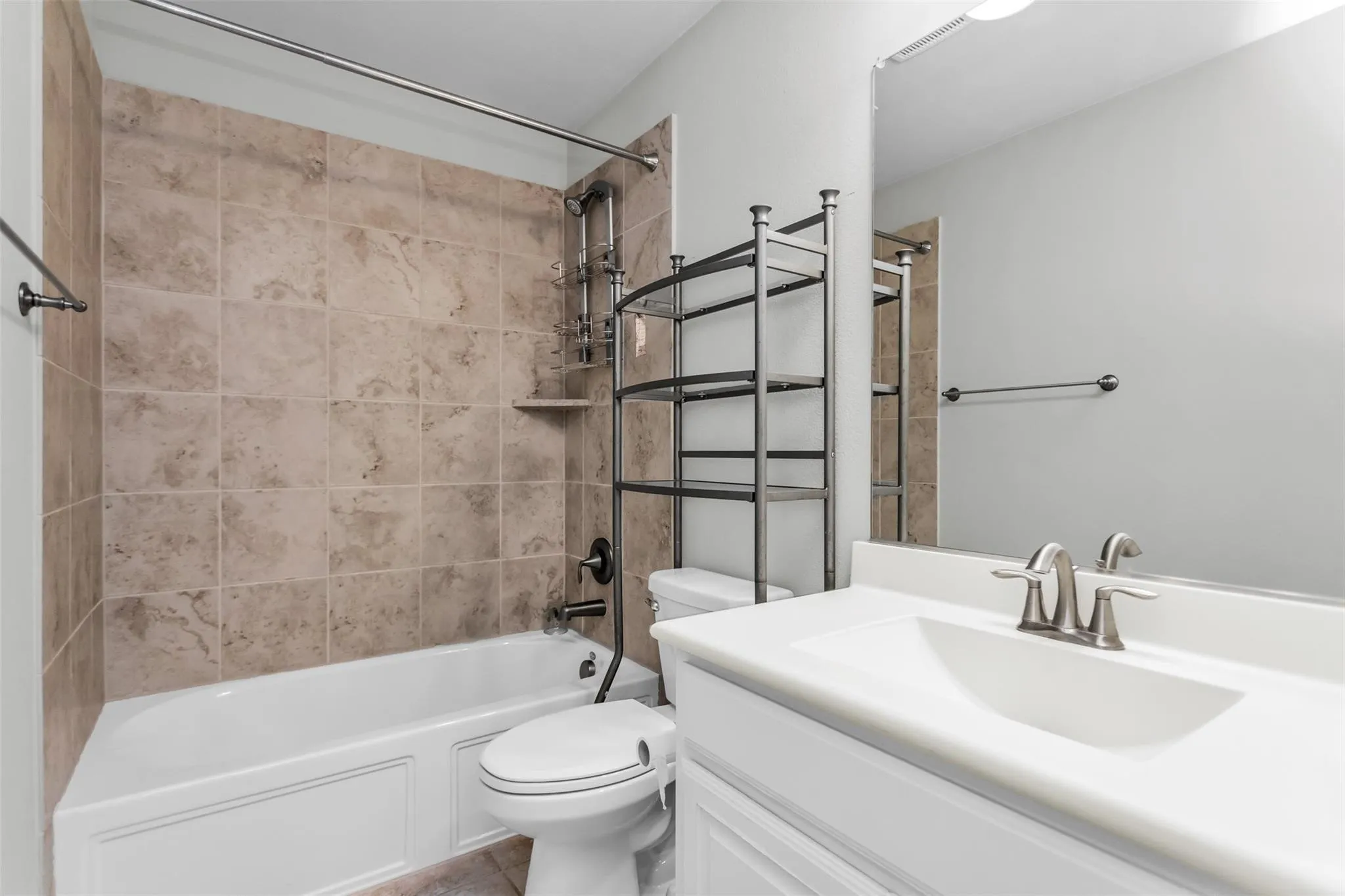 Bathroom featuring a white vanity with an integrated sink, brushed nickel faucet, large wall mirror, and a shower-tub combination with natural stone tile surround