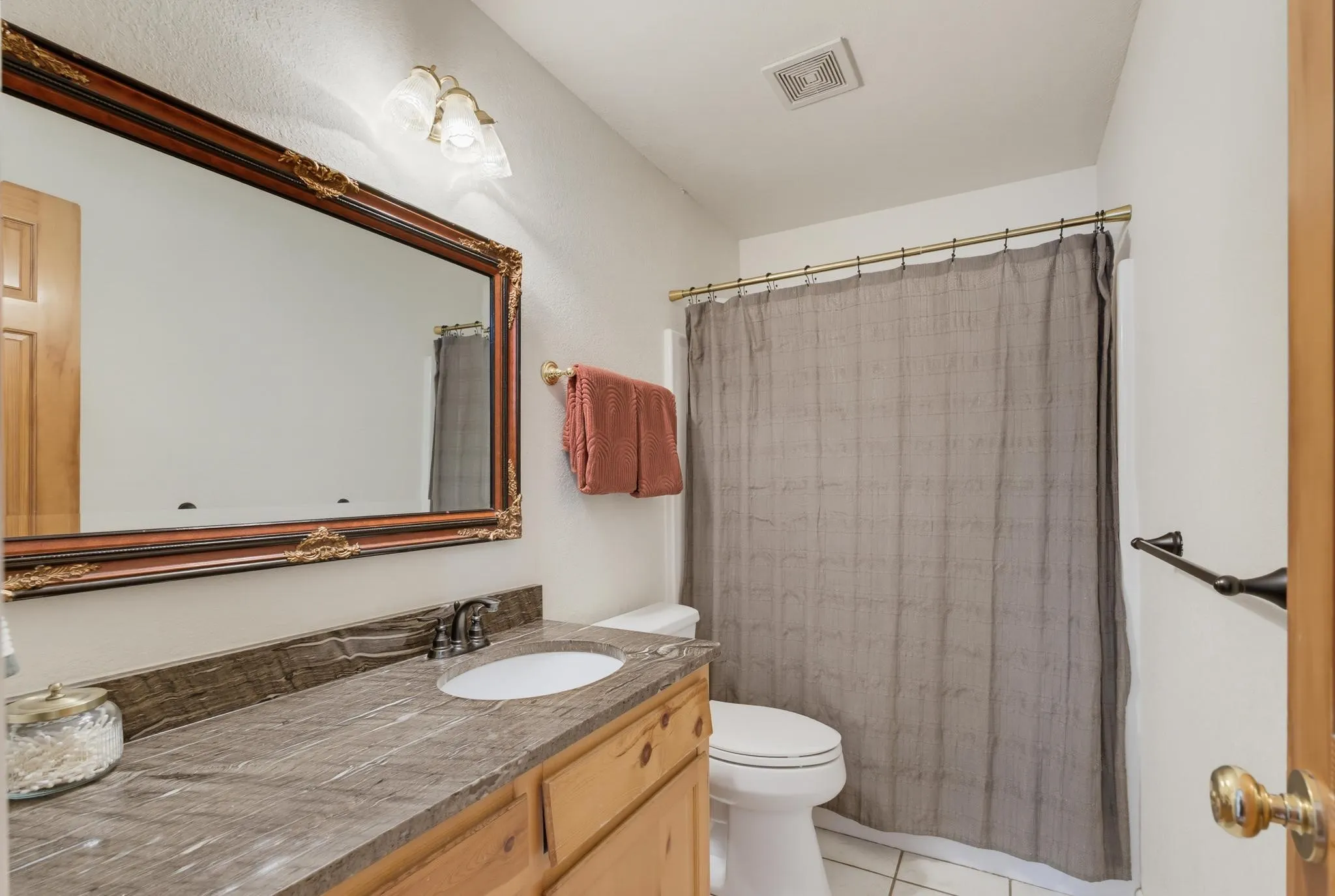 Wood-finish vanity with a single basin sink, stone-finish countertop, and decorative framed mirror