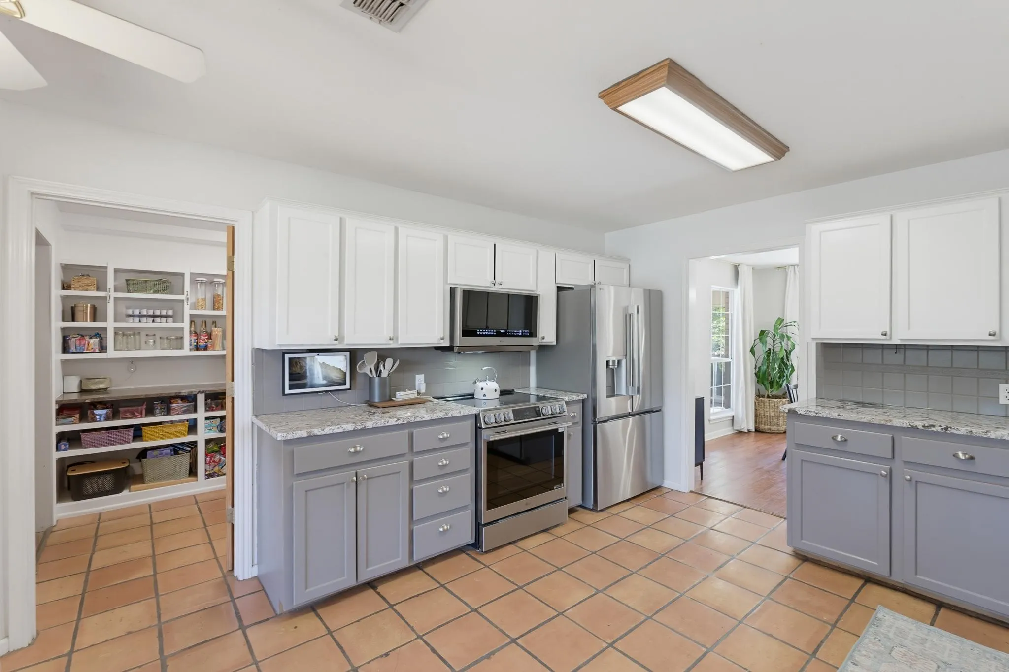 Kitchen featuring tile flooring, two-tone cabinetry with upper white and lower gray finishes, light-toned countertops, and stainless steel appliances