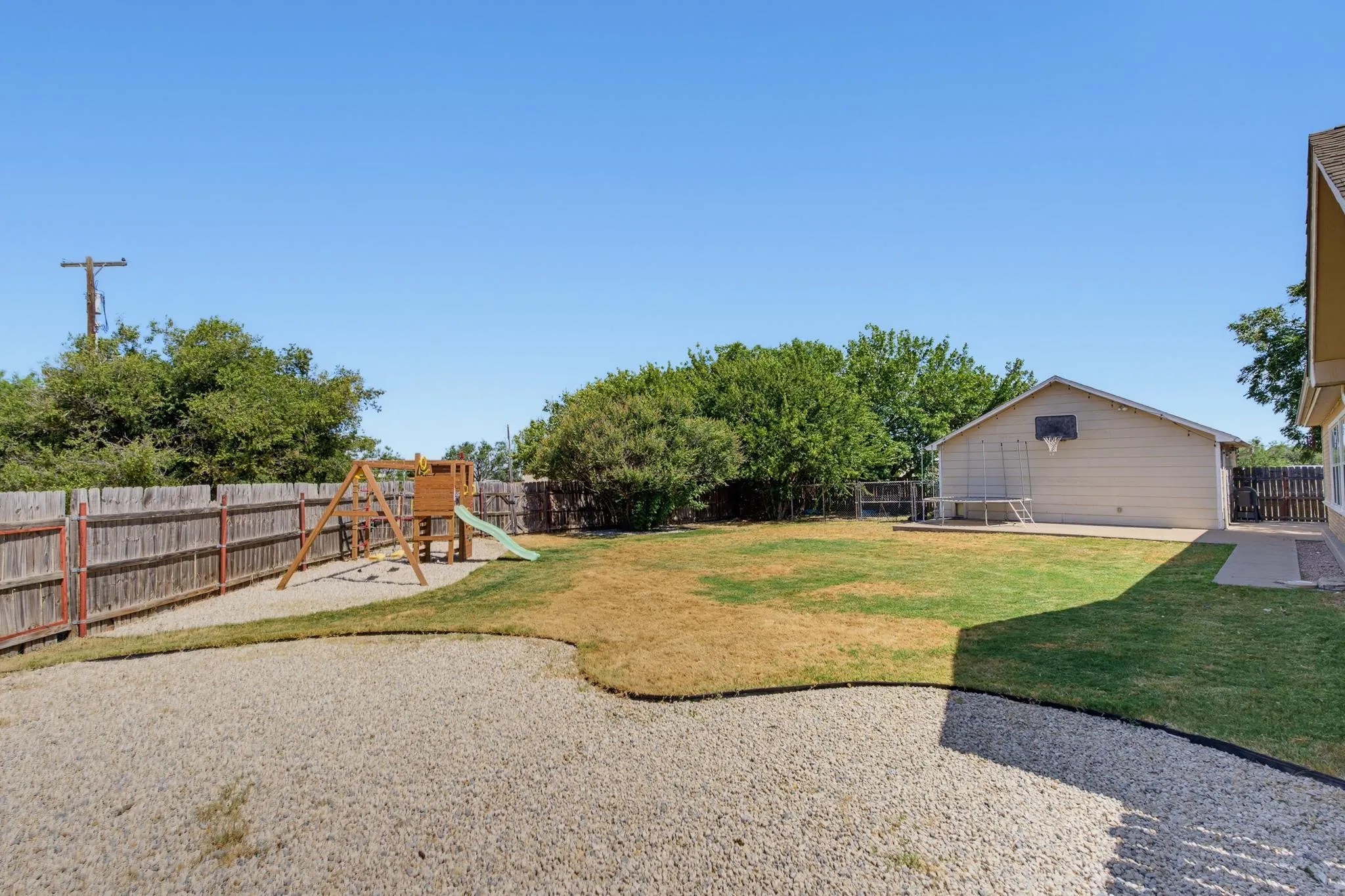 Expansive backyard featuring a large gravel area, a grass lawn, and a wooden privacy fence