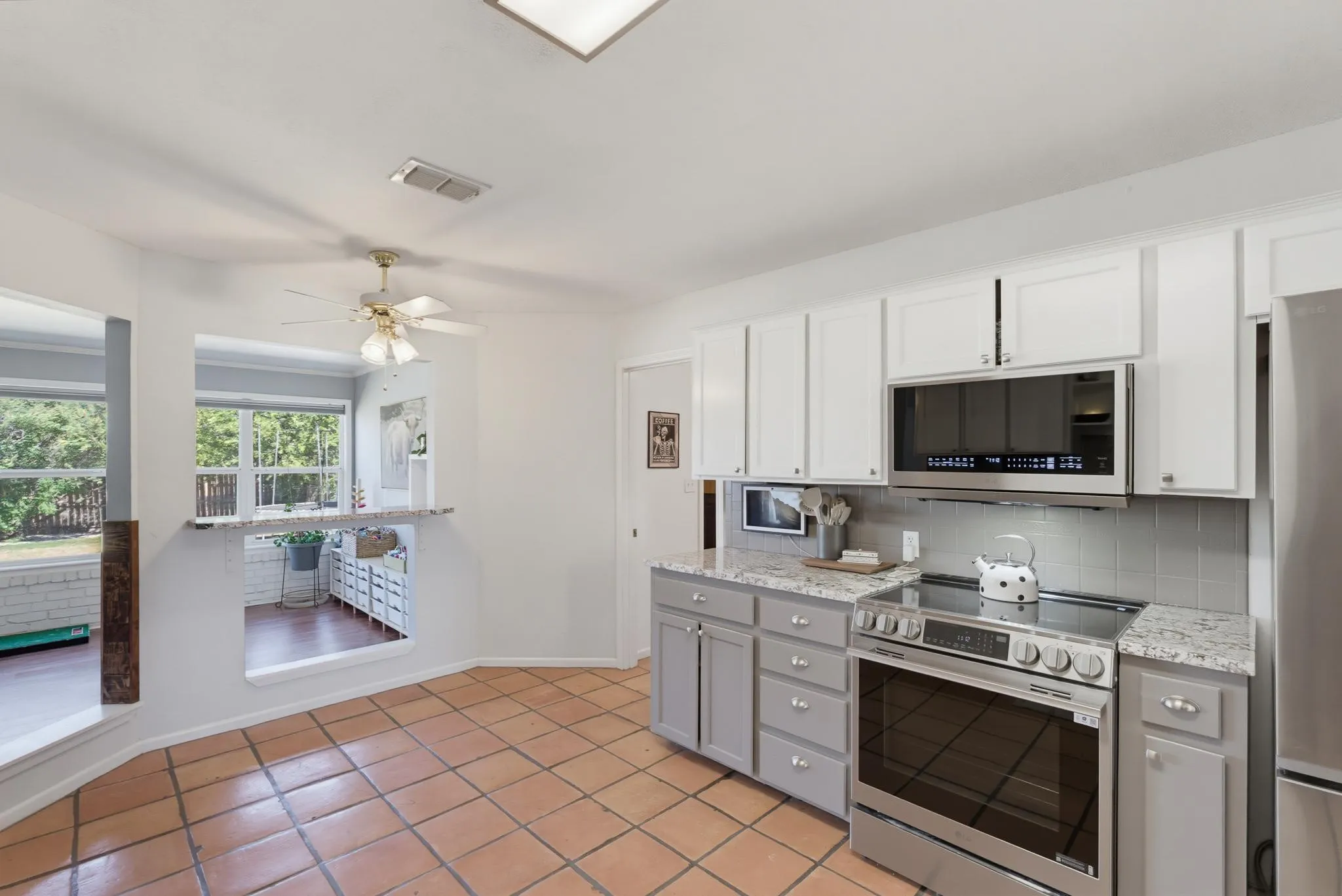Kitchen featuring stainless steel appliances, white upper cabinetry, gray lower cabinetry, and light-toned countertops