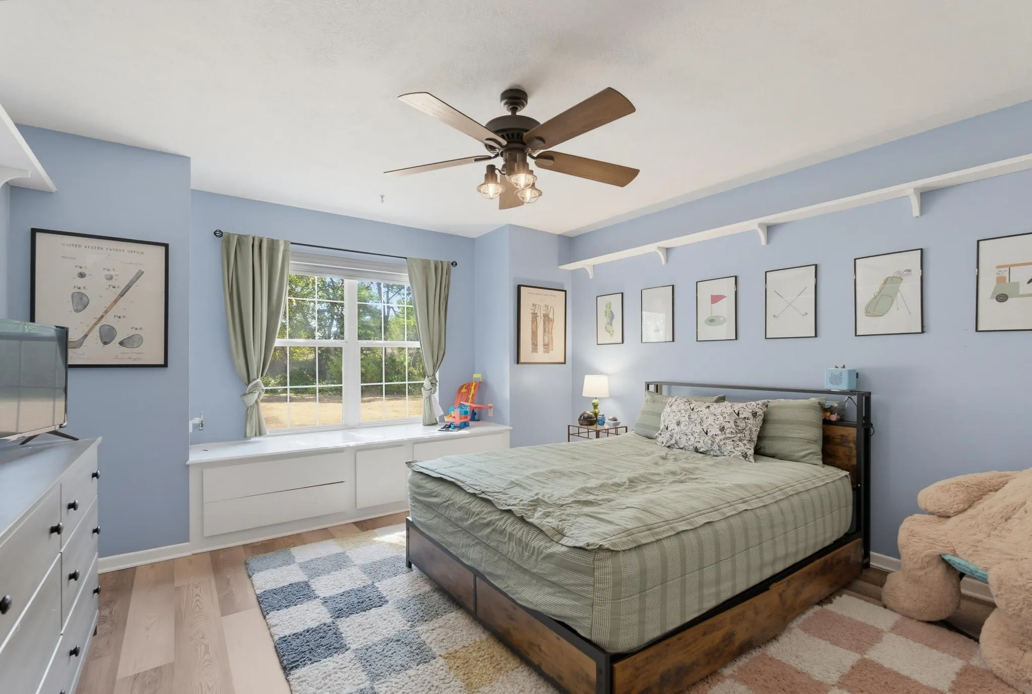 Room featuring wood-finish flooring, a window with natural light, a ceiling fan with integrated lighting, and built-in shelving