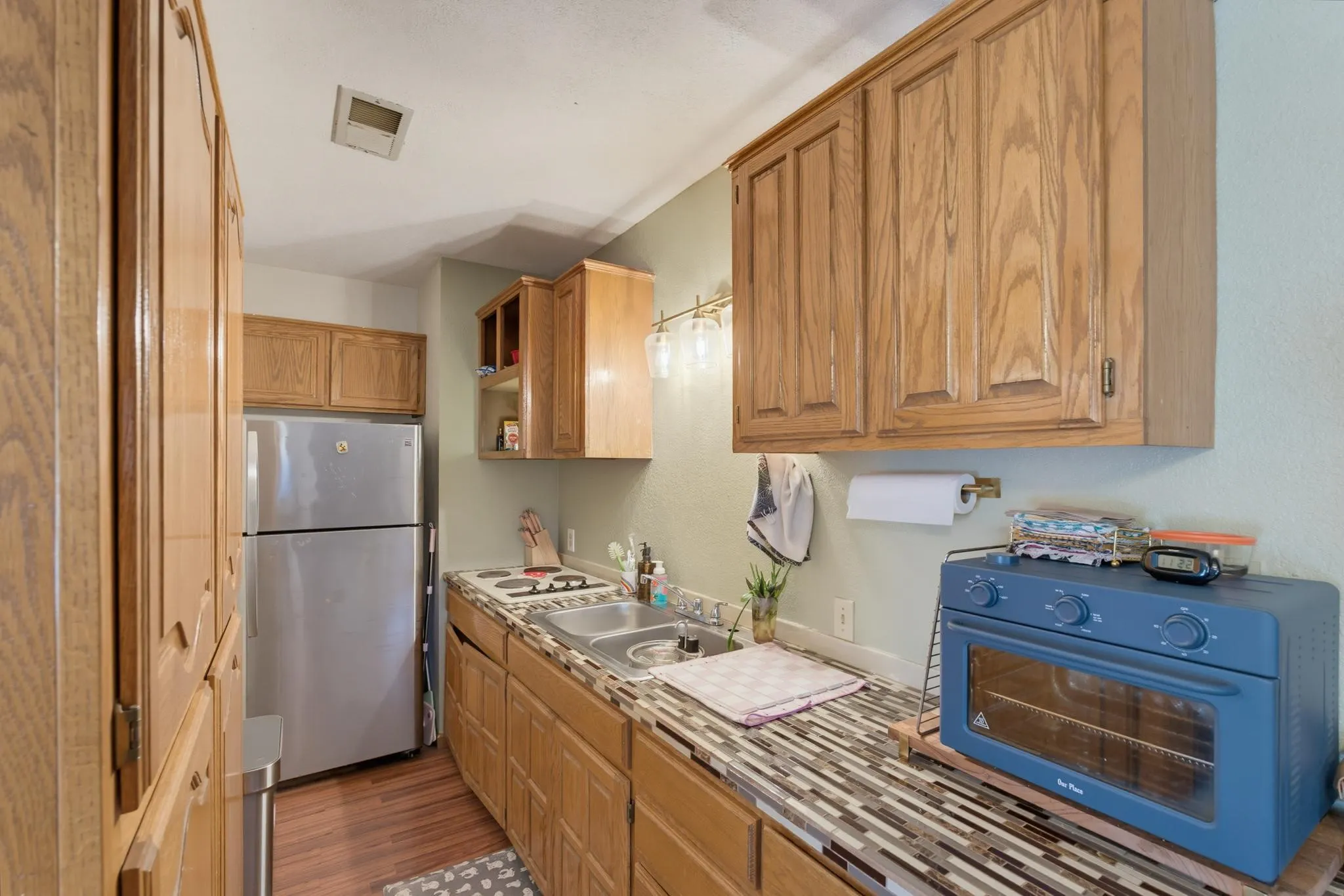 Apartment Kitchenette featuring wood-finish cabinetry, stainless steel refrigerator, tile backsplash, stainless steel sink, and wood-finish flooring