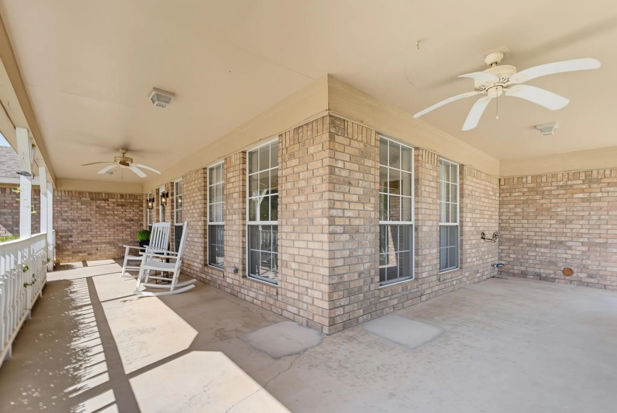 Expansive covered patio featuring brick exterior, multiple windows, and two ceiling fans