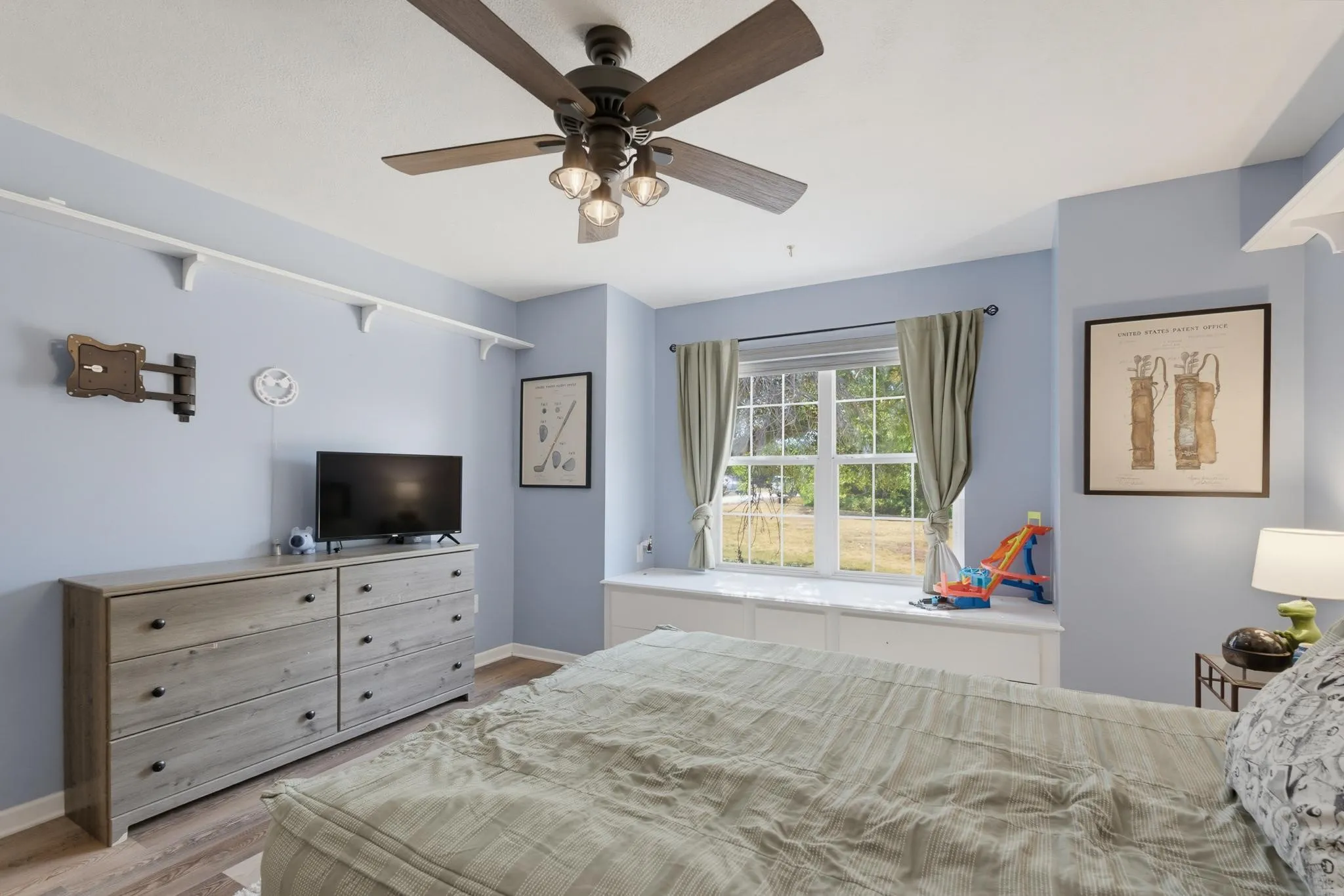 Ceiling fan with integrated lighting, large window with natural light, built-in window bench with storage, and wood-finish flooring
