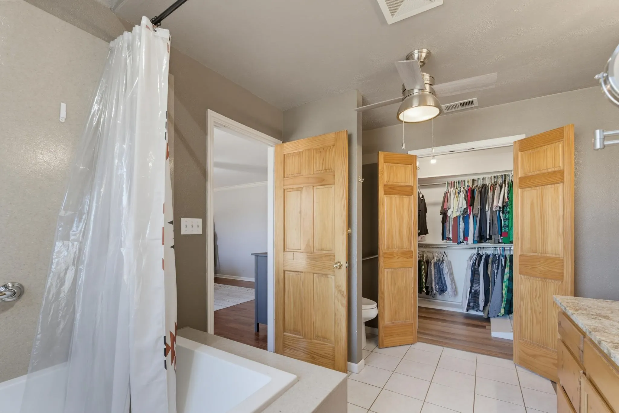 Built-in tub with tile surround, wood-finish bi-fold closet doors, and tile flooring
