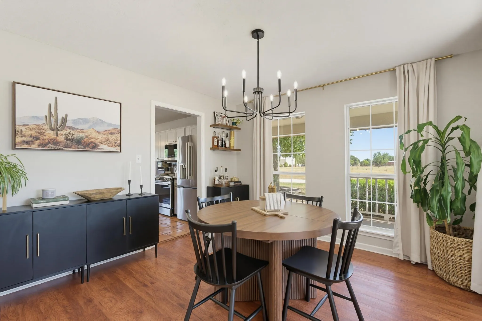 Wood-finish flooring, a contemporary chandelier, two large windows, a built-in shelving unit, and an arched doorway