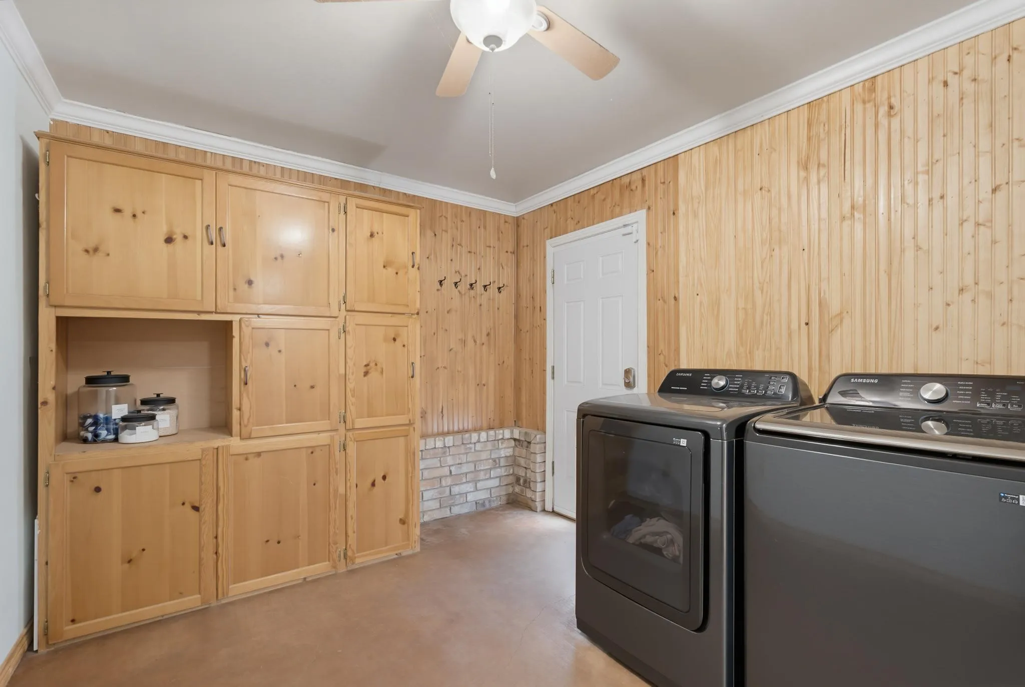 Built-in cabinetry, wood-paneled walls, brick wainscoting, and a ceiling fan