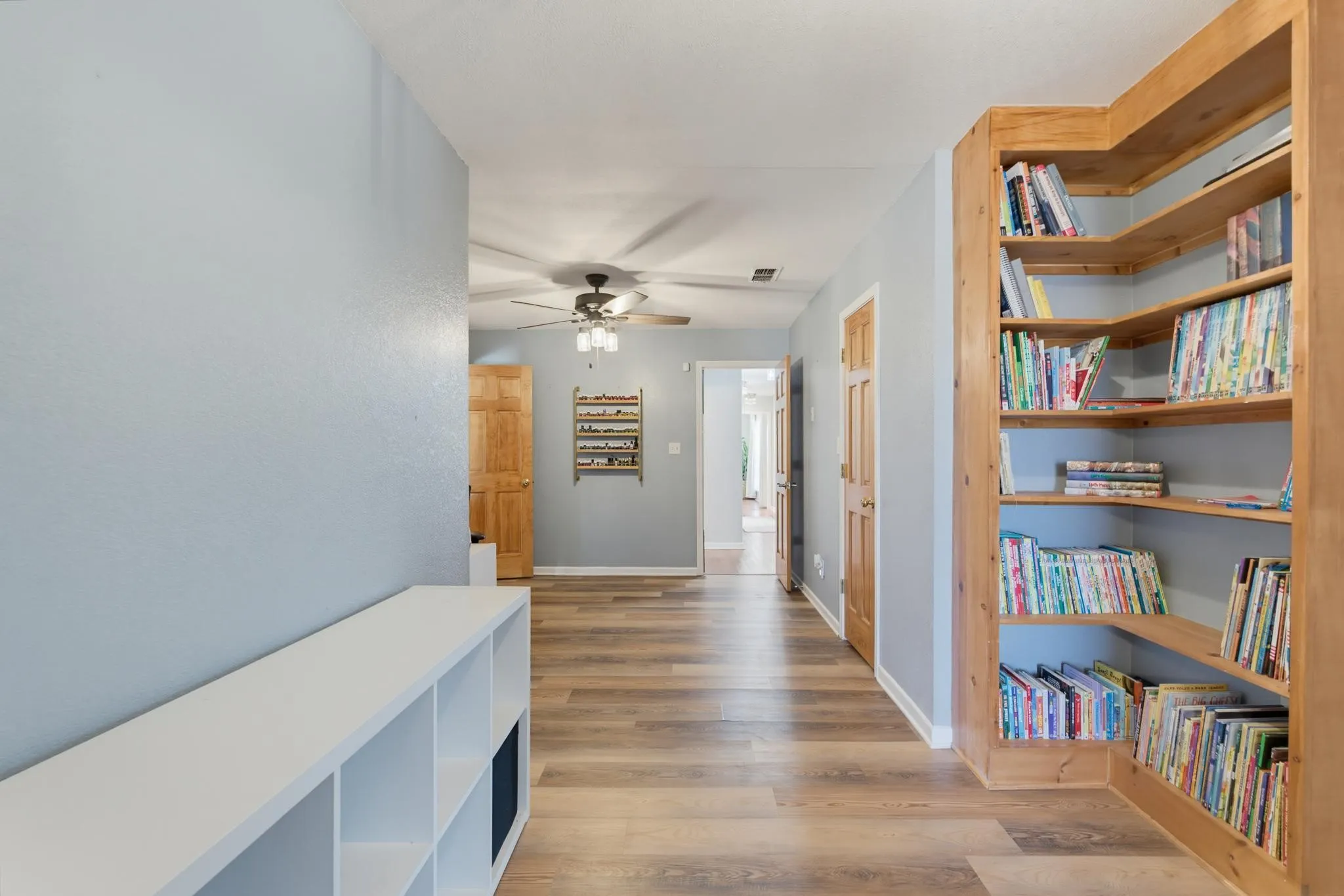 Wood-finish flooring, light blue wall paint, natural wood doors, a built-in wood bookshelf, and a white storage bench