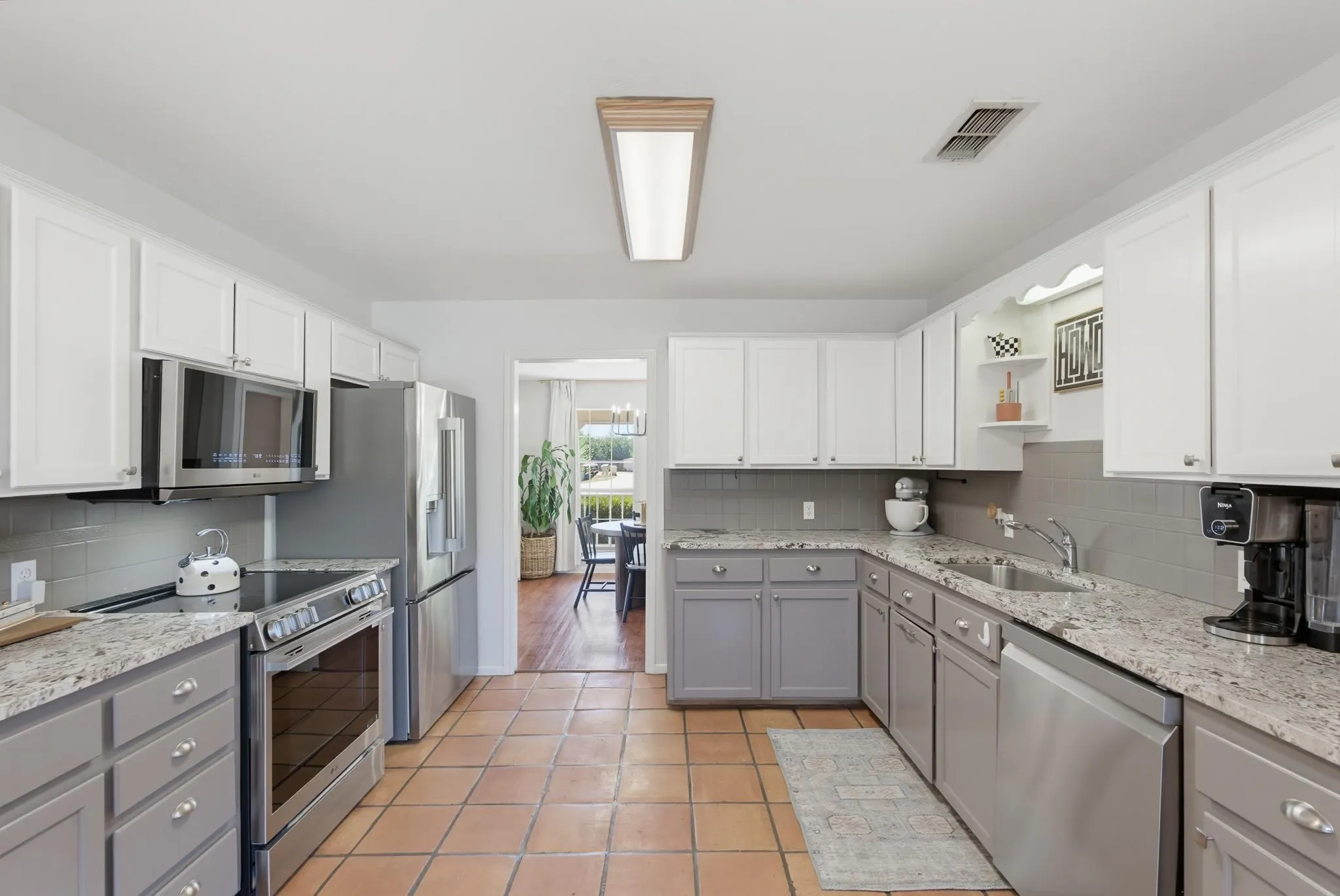 Two-tone cabinetry with white upper and gray lower units, stainless steel appliances, speckled stone countertops, and a gray subway tile backsplash