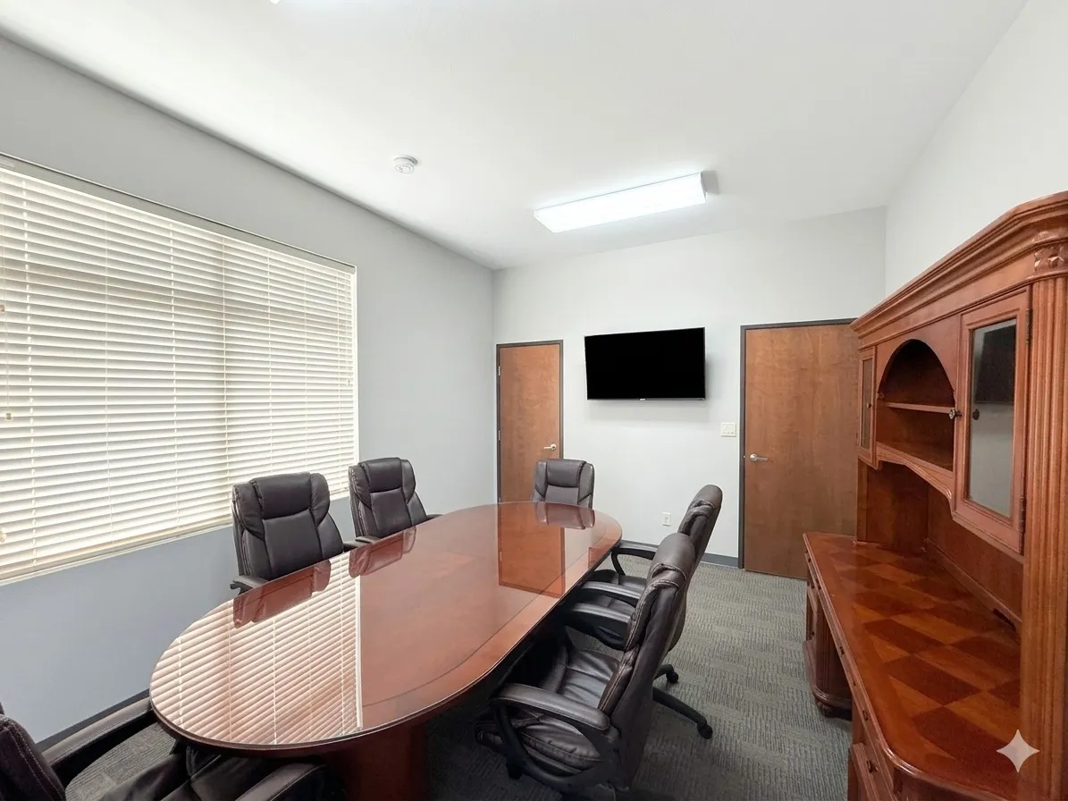 Conference room with light gray walls, wood-finish doors, wall-mounted display, and carpeted flooring