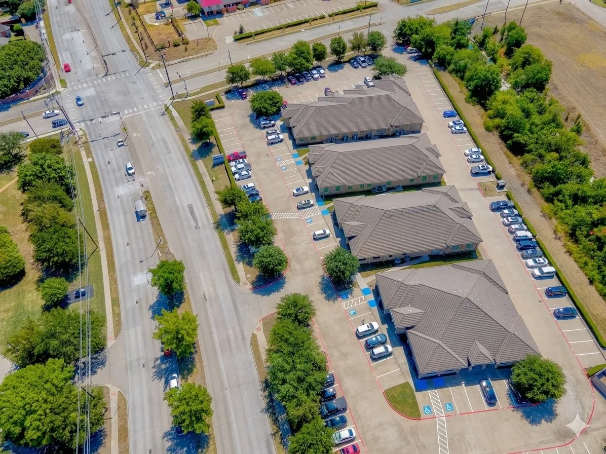 Three commercial buildings with ample paved parking, surrounded by mature trees, and situated adjacent to a multi-lane thoroughfare