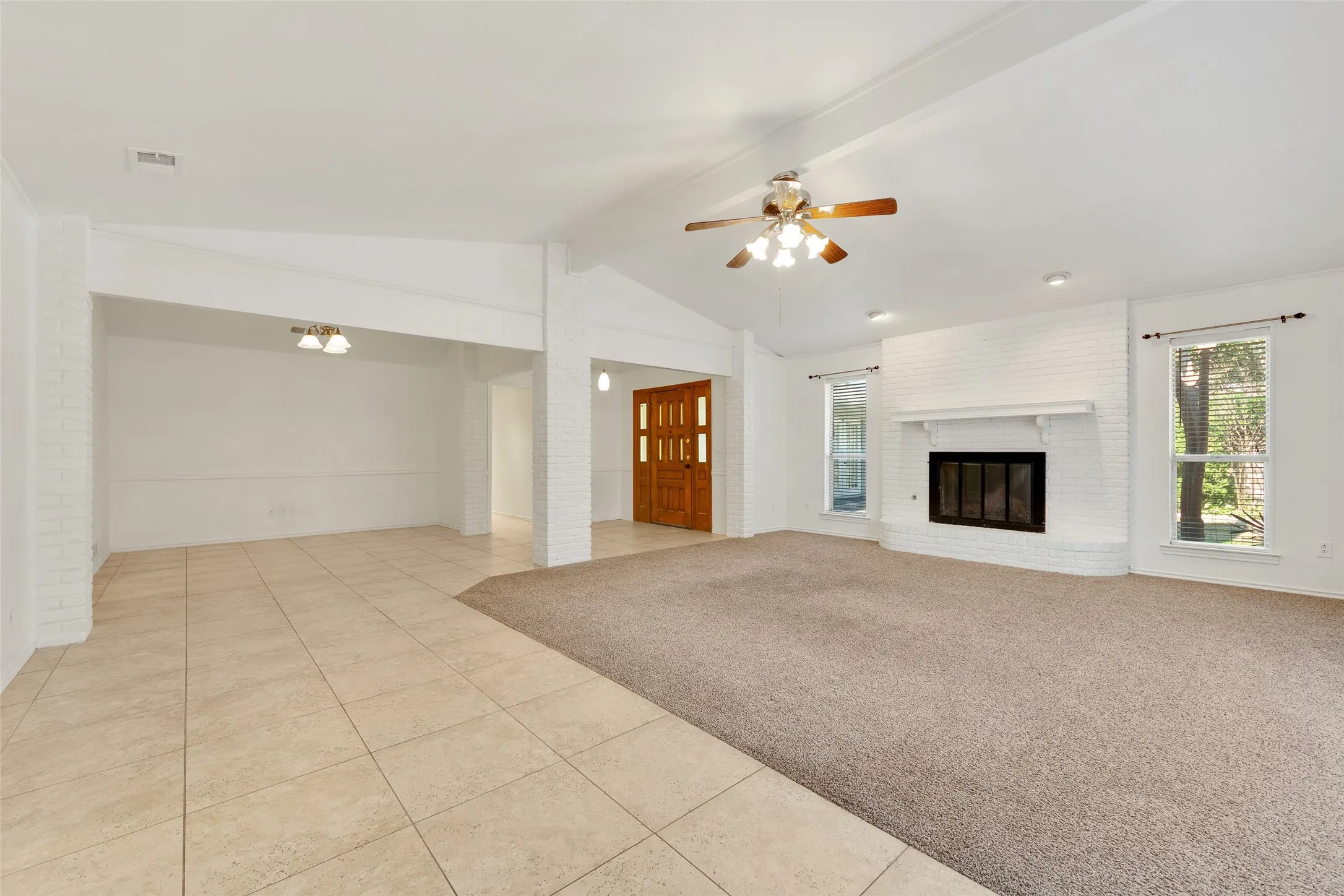 Spacious living area featuring a white brick fireplace, multiple windows, and a ceiling fan