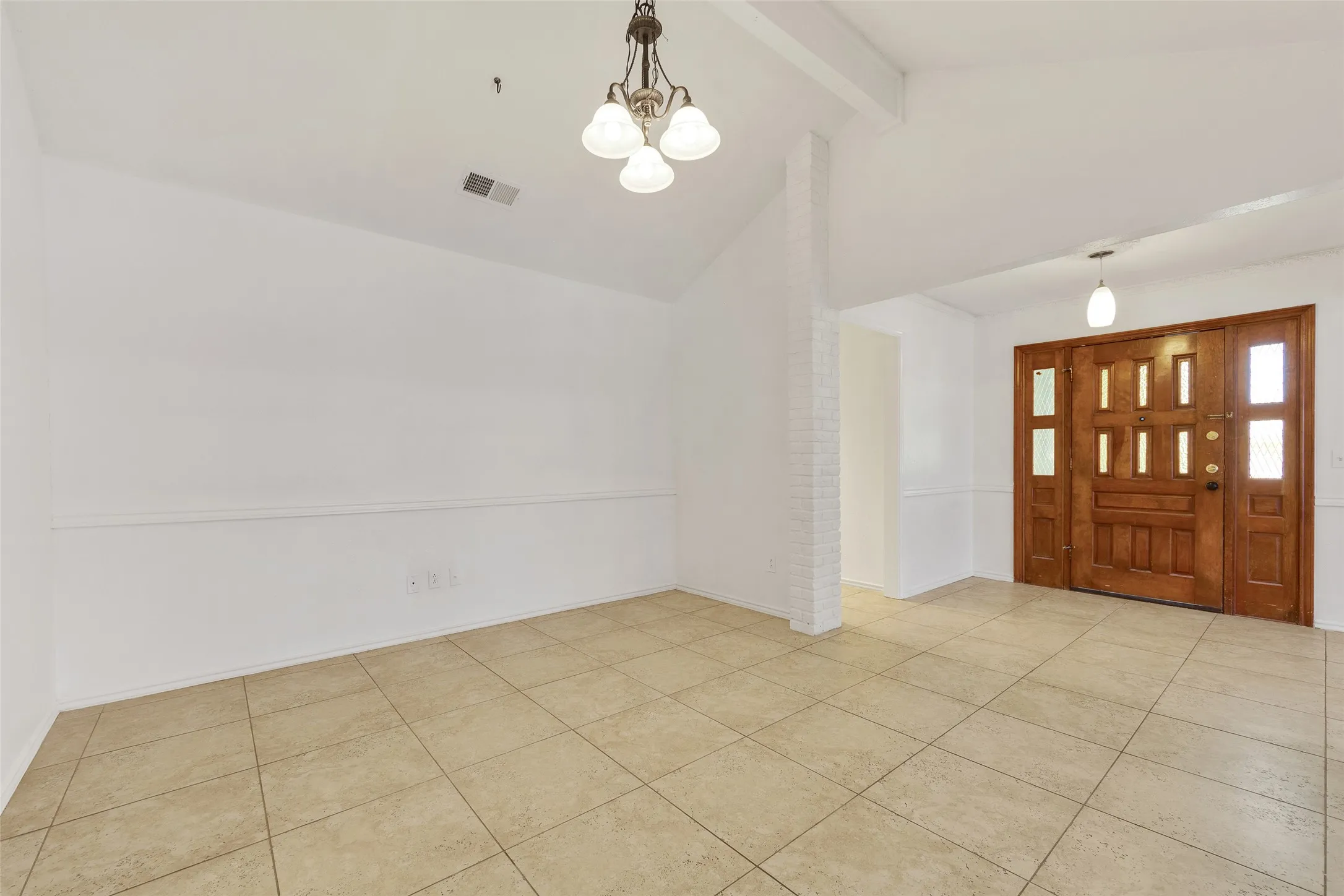 Entryway featuring a paneled wood-finish door with sidelights, tile flooring, vaulted ceiling, and an exposed brick accent wall