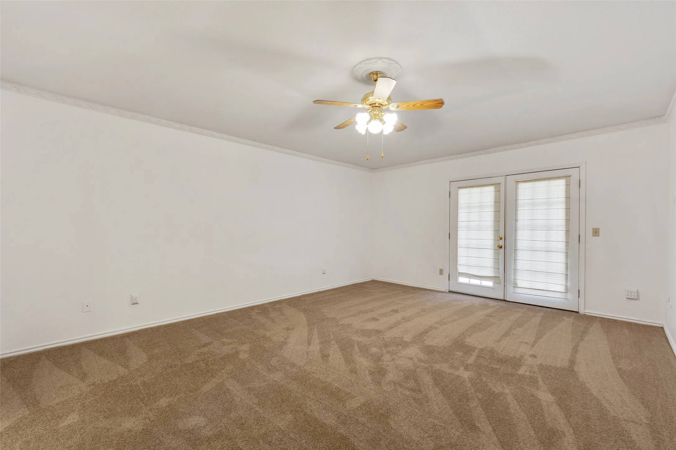 Double French doors, ceiling fan with integrated lighting, crown molding, and neutral-toned carpeting