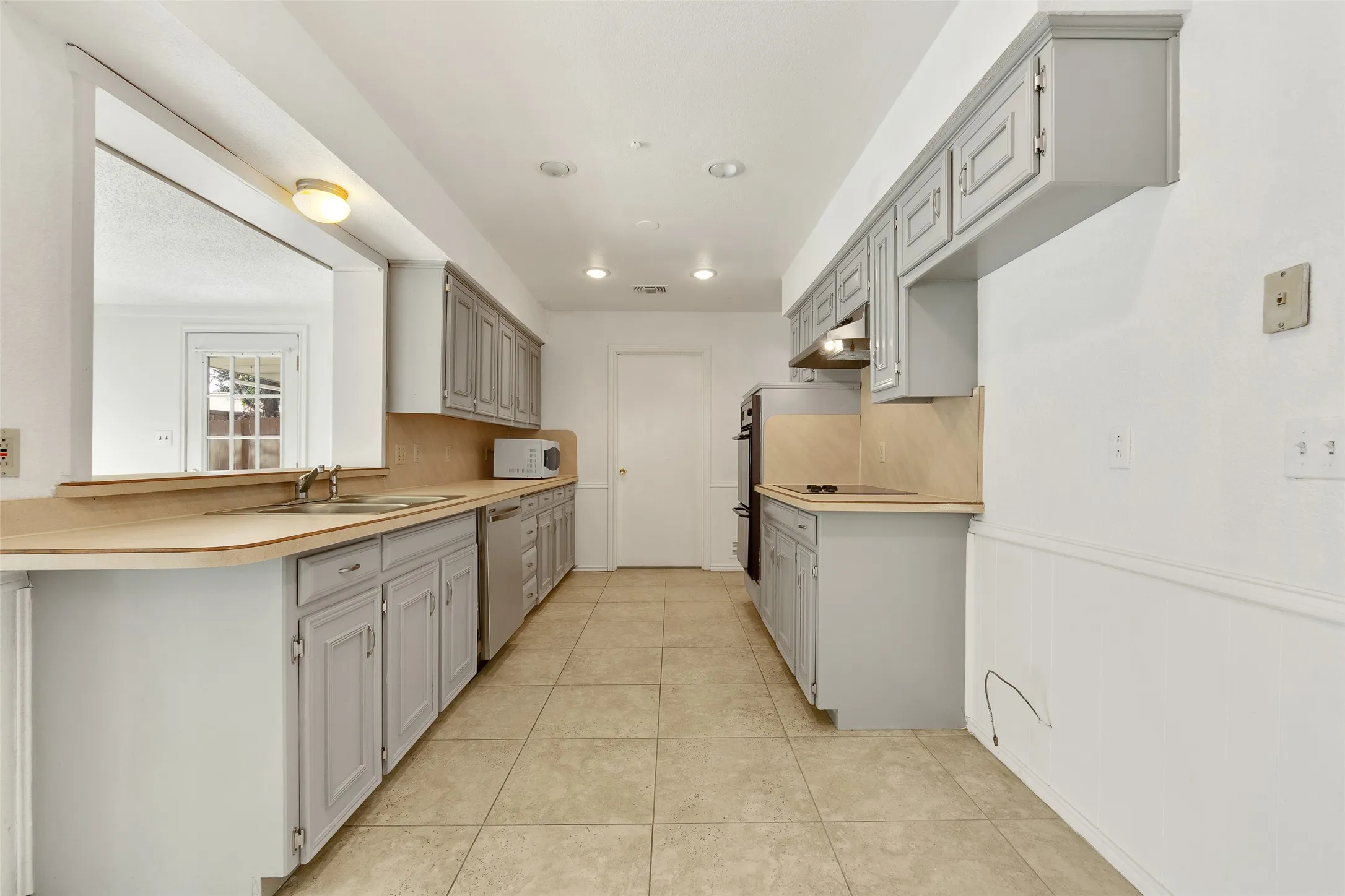 Kitchen with tile flooring, gray cabinetry, built-in appliances, and a pass-through window