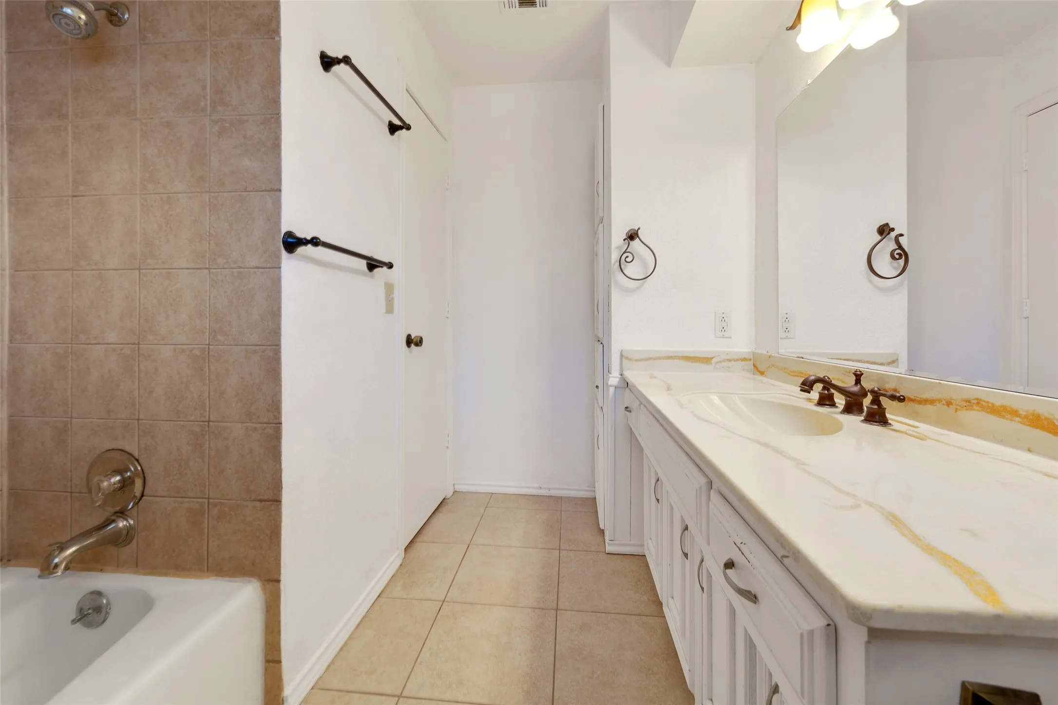 Dual sink vanity with an integrated countertop, tile flooring, and a shower-over-tub combination with tile surround