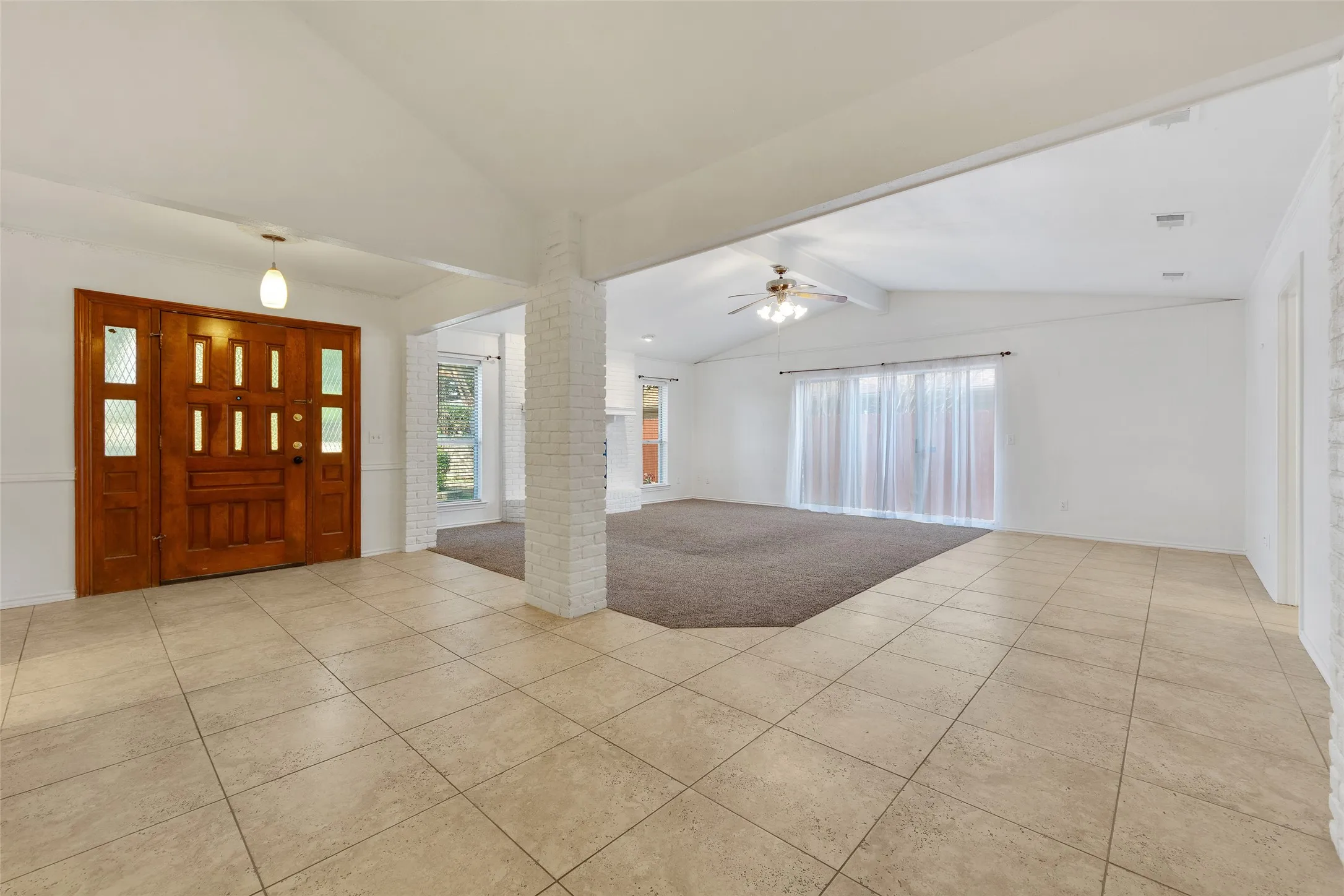 Tiled entryway with a wood-paneled door, leading to a living space with vaulted ceilings and a ceiling fan