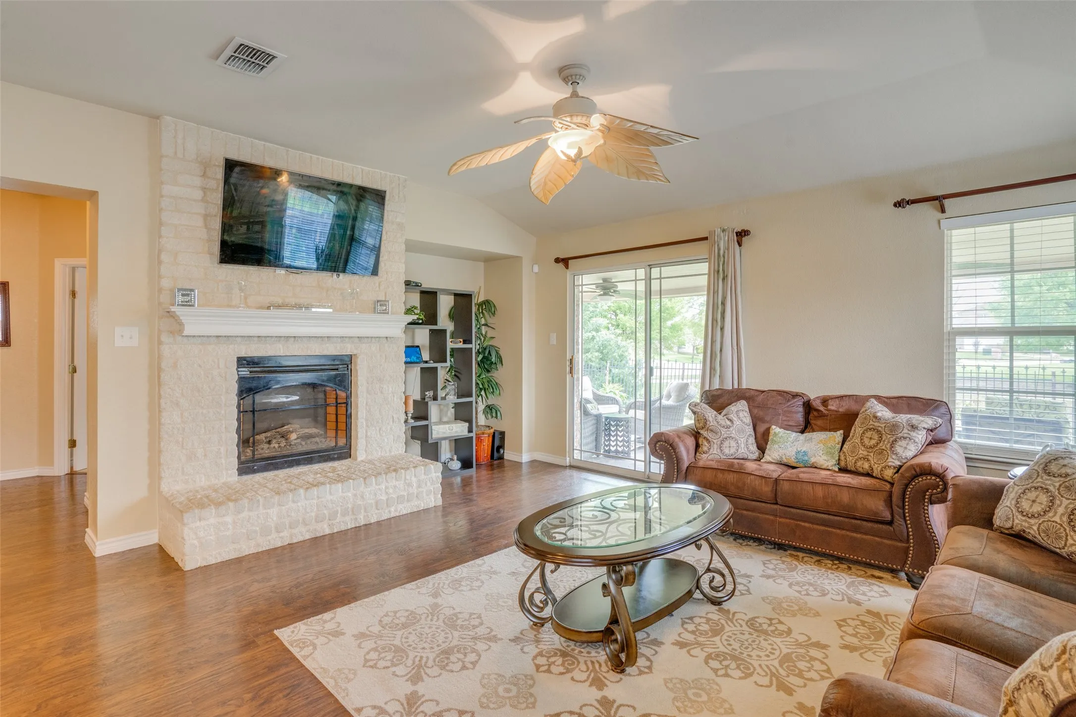 Living area featuring a stone-clad fireplace with a mantel, vaulted ceiling with a ceiling fan, and wood-finish flooring