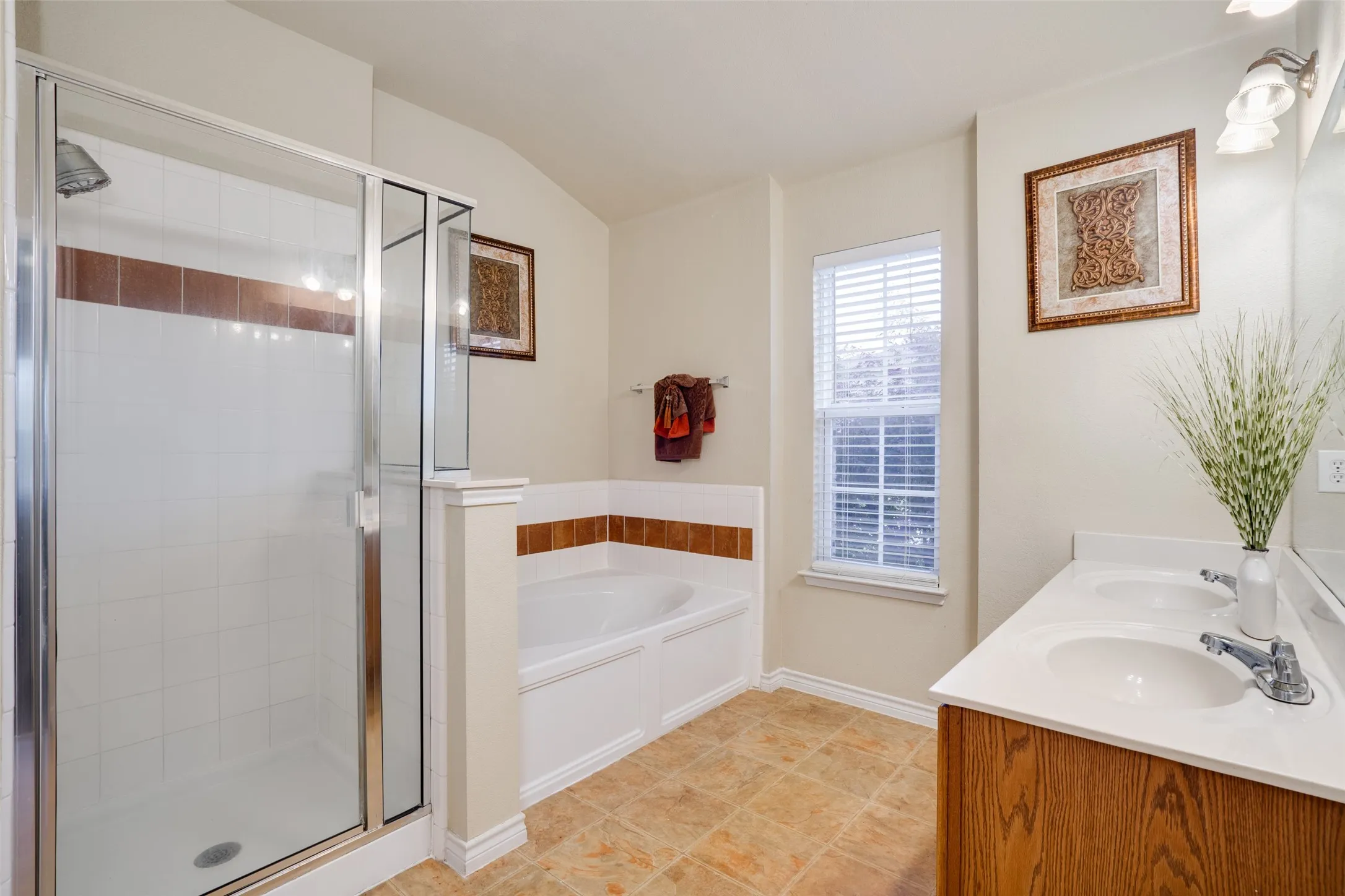 Tiled flooring with a white-tiled shower enclosure, a built-in bathtub, a window with blinds, and a double vanity with an integrated sink