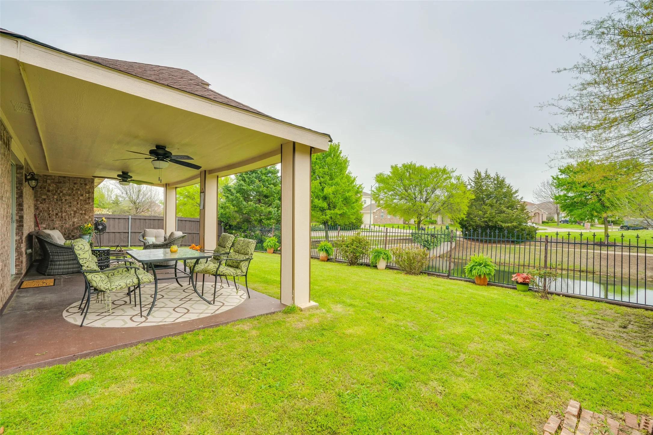 Expansive covered patio with dual ceiling fans, brick exterior detailing, and a manicured lawn