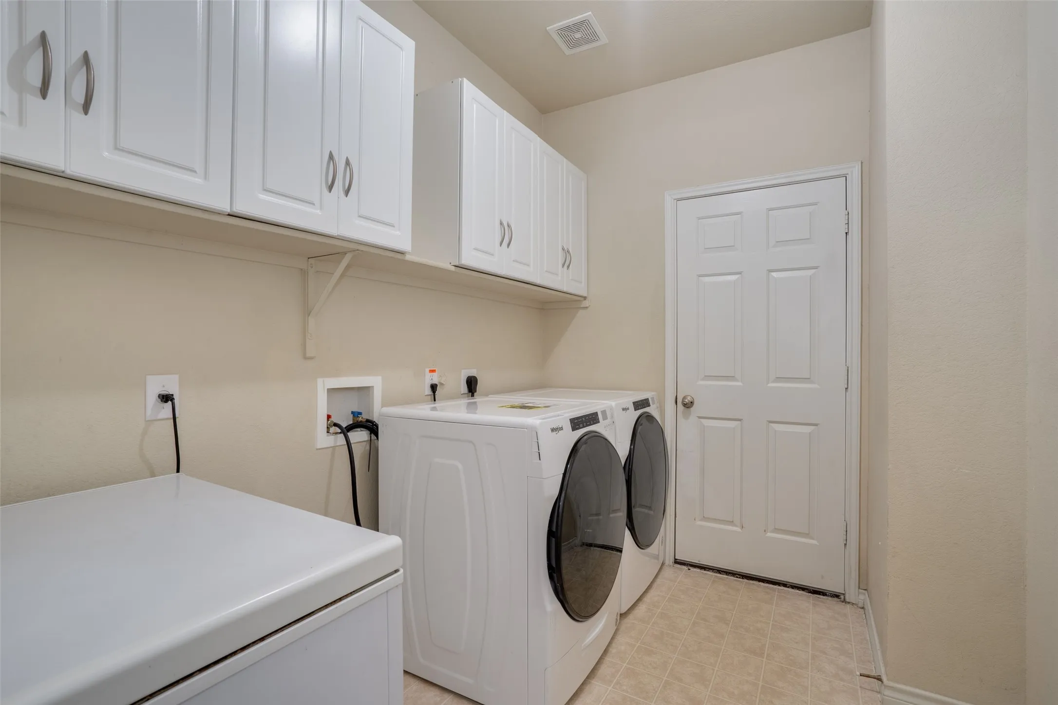 White upper cabinetry with brushed nickel hardware, light neutral wall paint, and tiled flooring