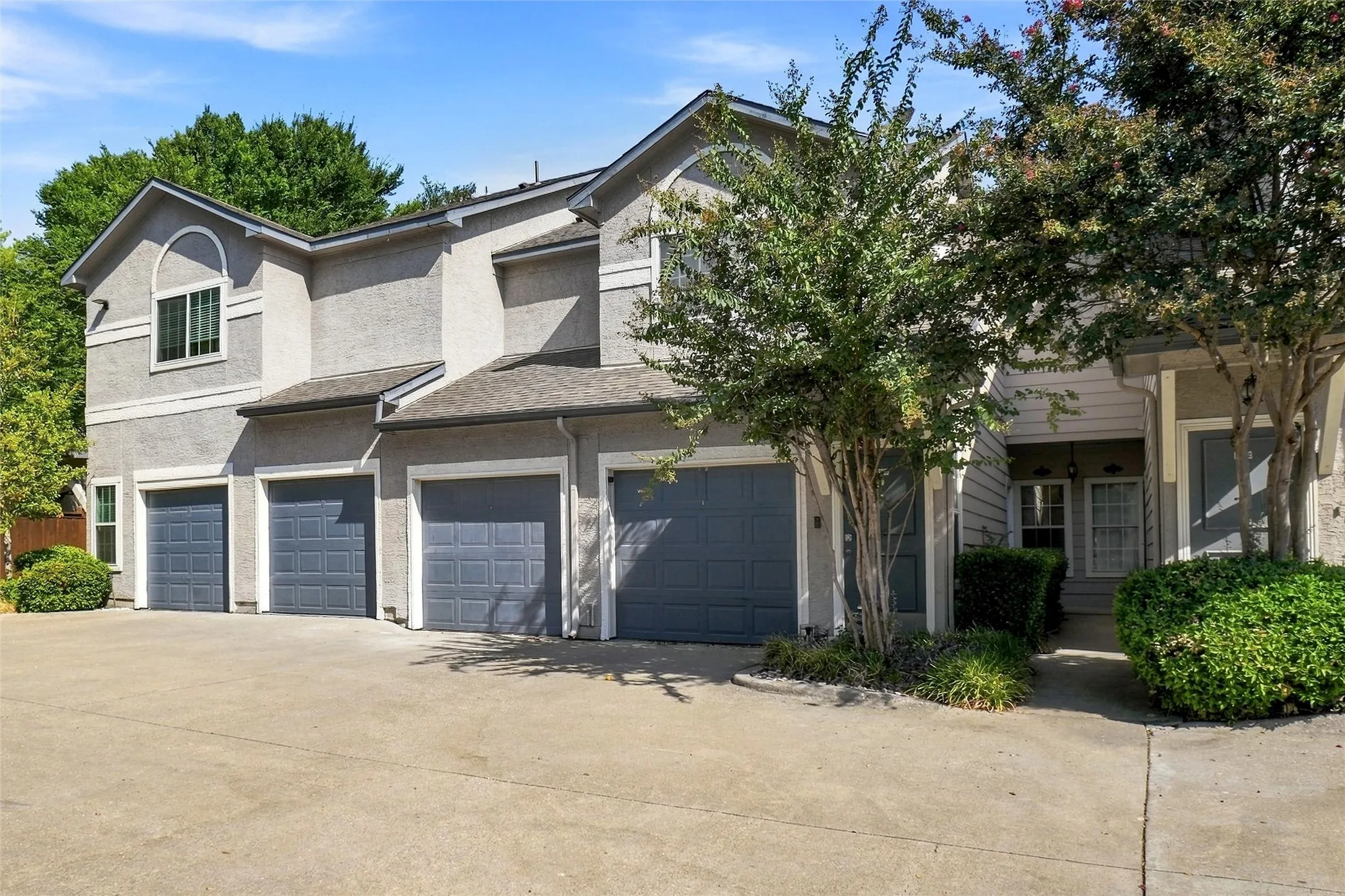Stucco exterior with multiple garage doors, arched window detail, and mature landscaping