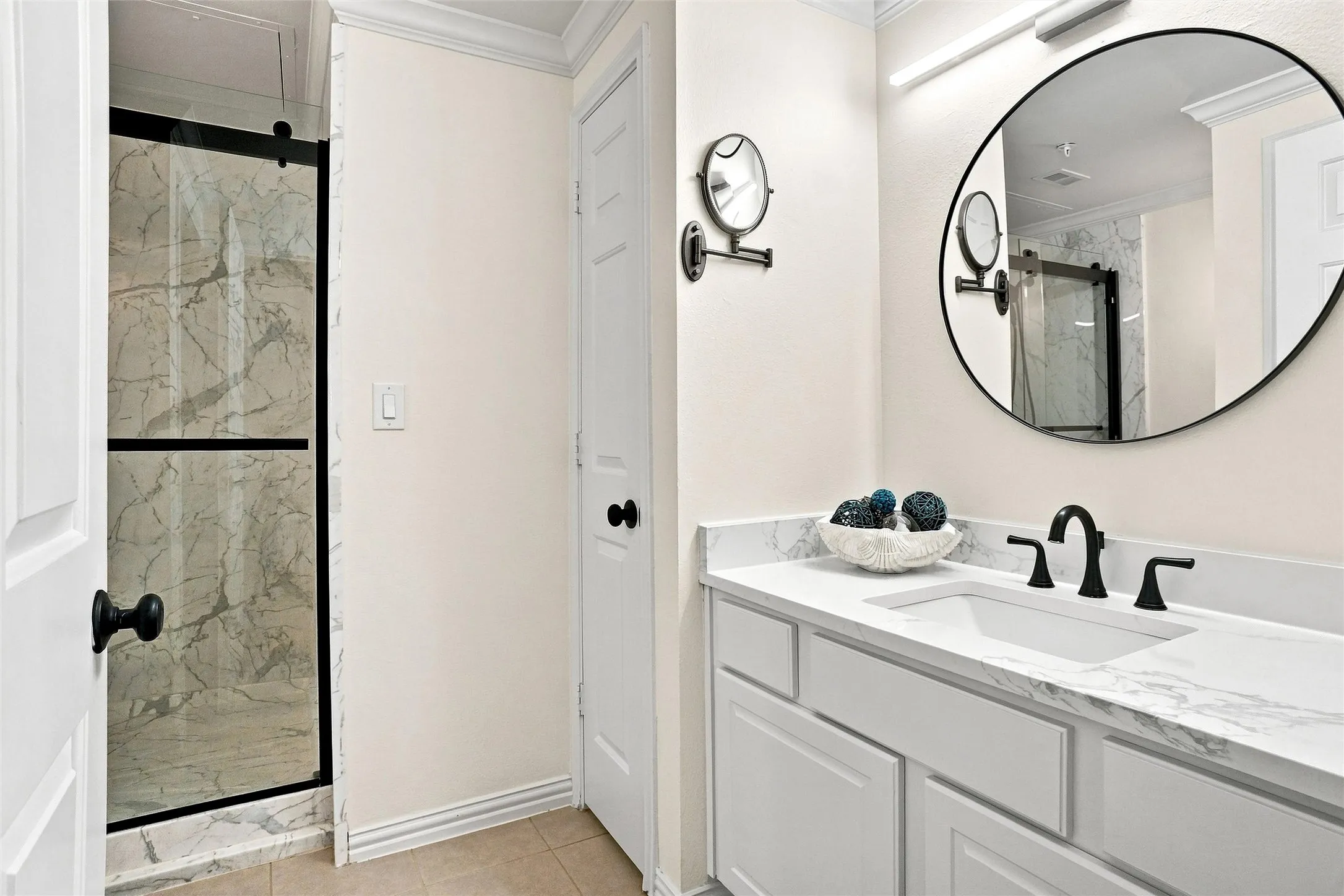 Shower with sliding glass enclosure, marble-style tile surround, and black hardware