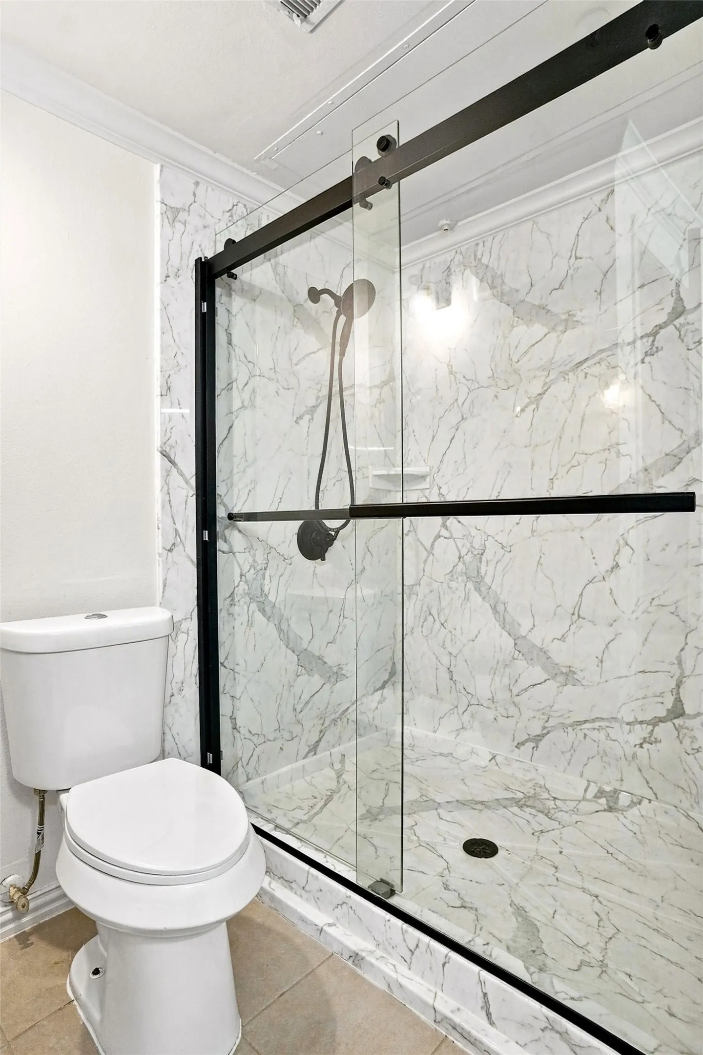 Shower enclosure with clear glass and matte black hardware, featuring marble-finish wall and floor tiling