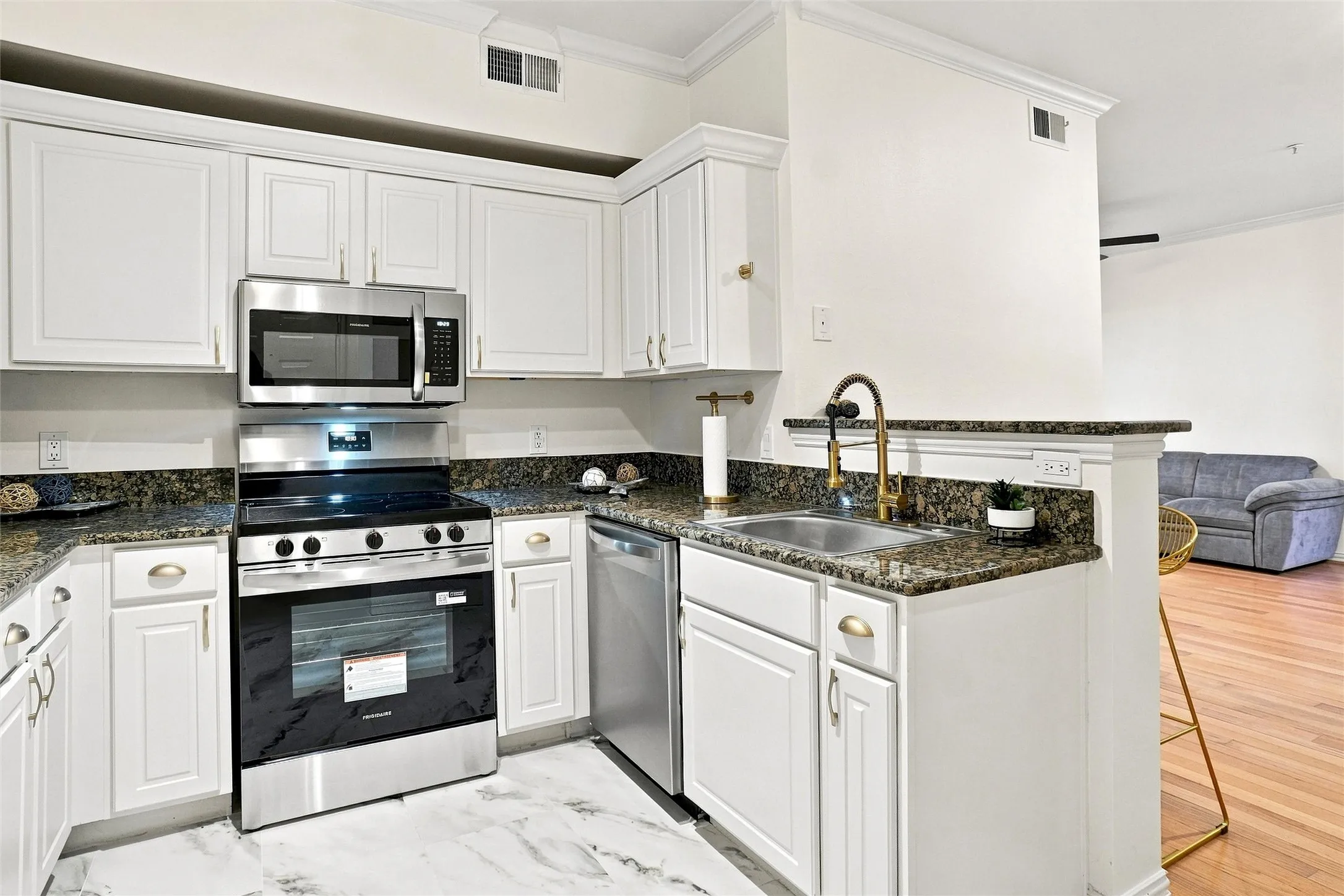 Kitchen featuring white cabinetry, stainless steel appliances, granite countertops, an undermount sink with a brass-finish faucet, and marble-look flooring