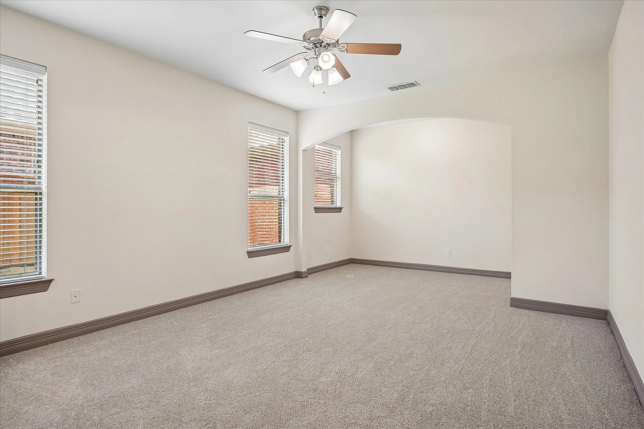 Carpeted room with a ceiling fan, multiple windows with blinds, and an arched doorway