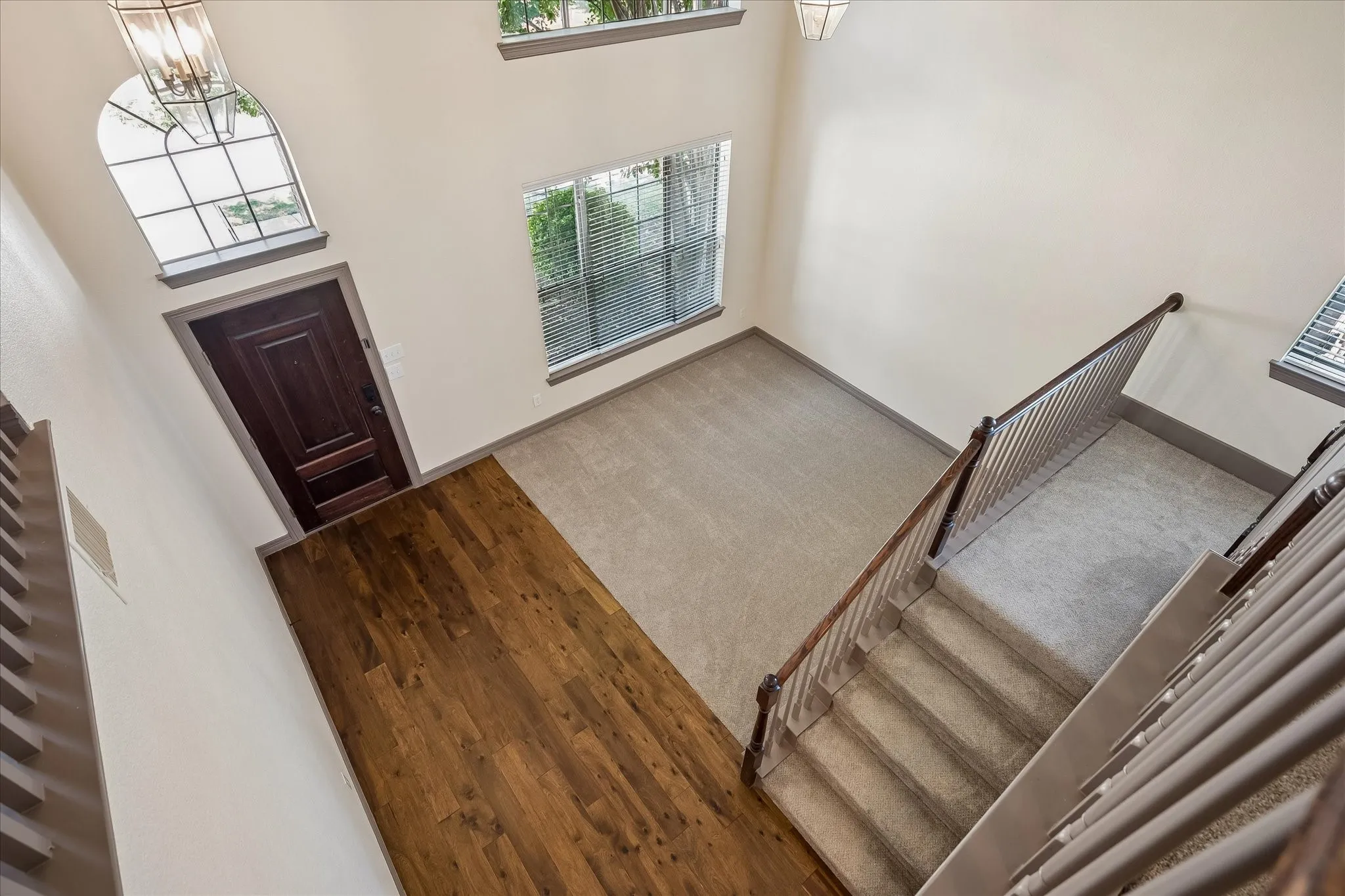 Two-story foyer with wood-finish flooring, arched window with transom, and a carpeted staircase with wood railing