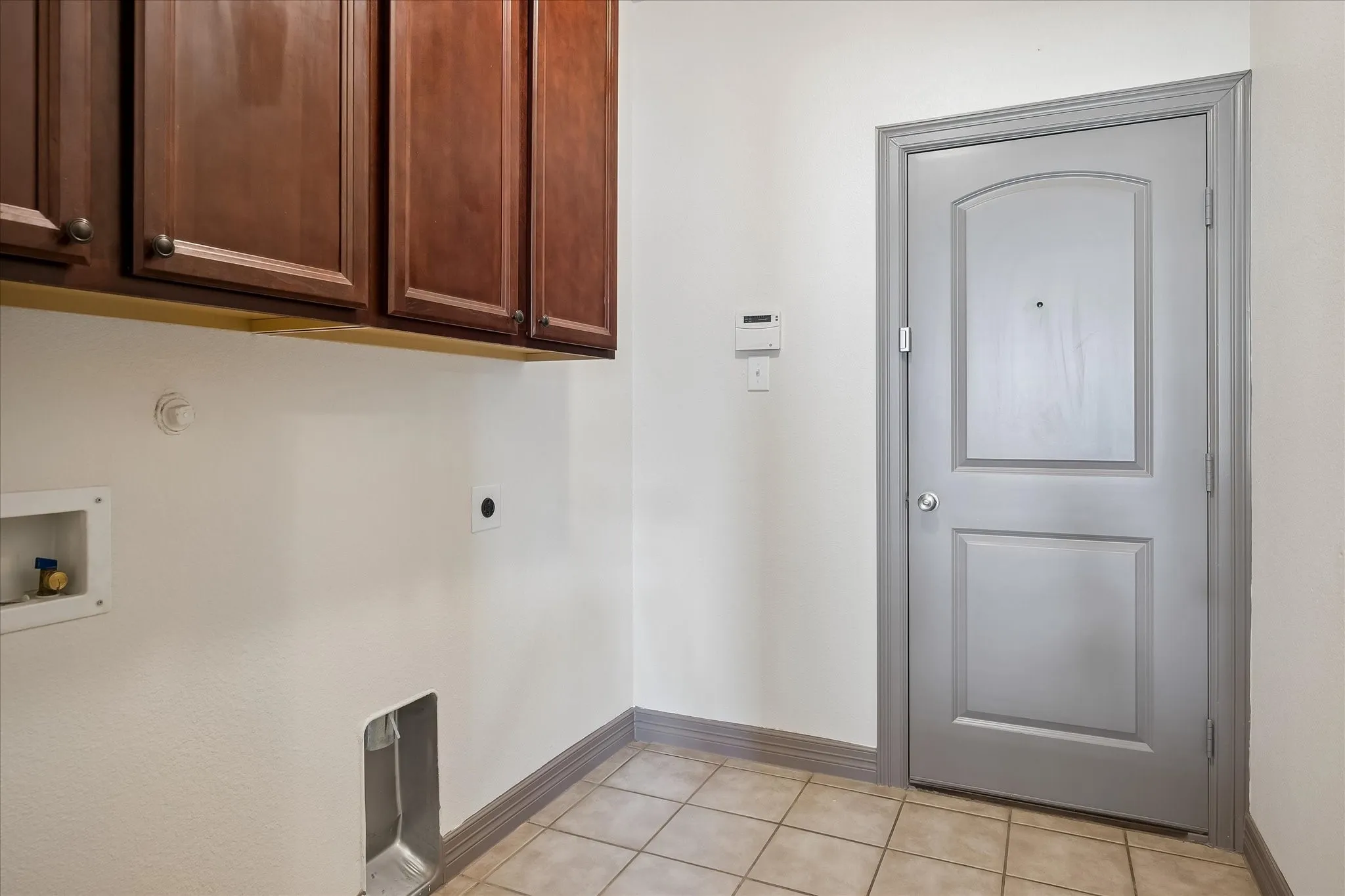Foyer with ceramic tile flooring, rich wood-finish cabinetry, and a gray-painted interior door featuring a two-panel design
