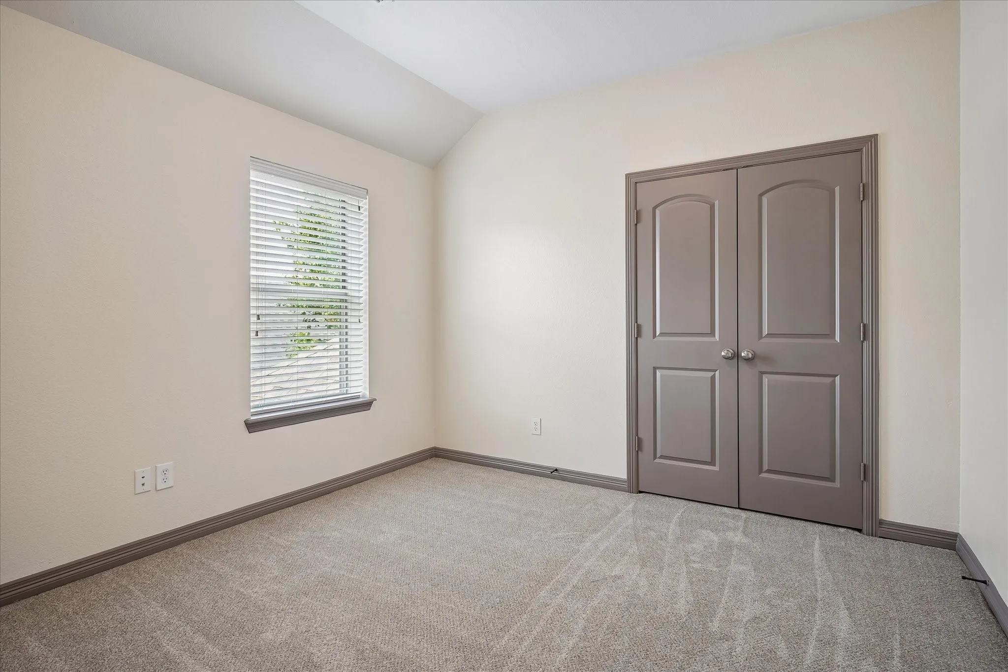 Vaulted ceiling accentuates the neutral color palette with carpet flooring and window blinds