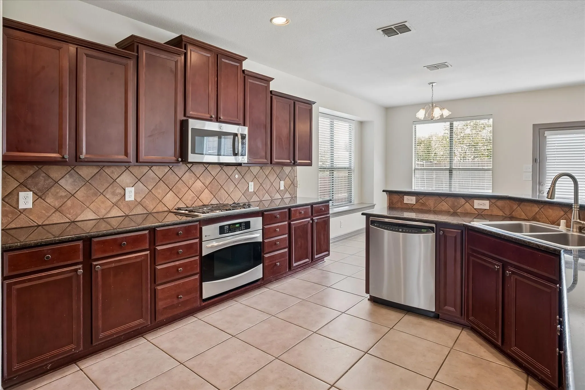 Elegant kitchen featuring rich cherry cabinetry with crown molding, stainless steel appliances including a built-in microwave and slide-in range, decorative tile backsplash, and contrasting countertops