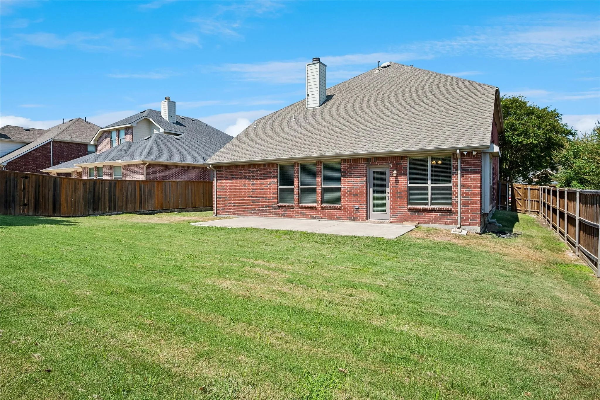 Expansive lawn with a full privacy fence, brick exterior, and a patio