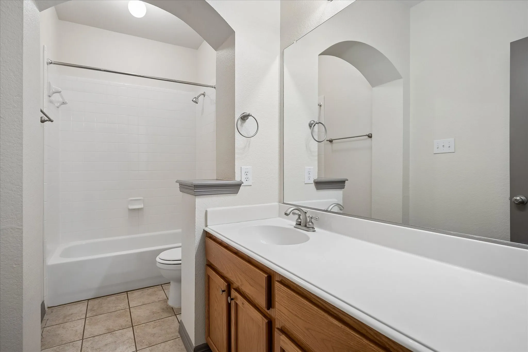 Bathroom featuring a white subway tile shower, built-in bathtub, wood-finish vanity with an integrated sink, and tile flooring